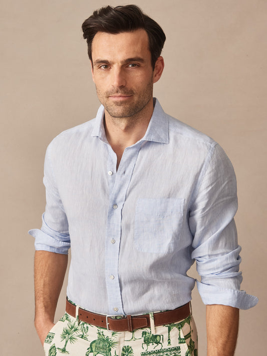Man wearing a light blue Gramercy Linen Shirt by J.McLaughlin, styled with a brown belt and patterned shorts, showcasing effortlessly stylish, enduring designs with innovative fabrics.