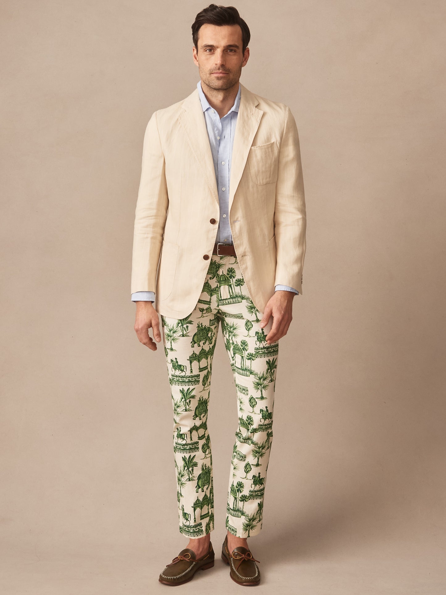Man wearing J.McLaughlin Brera Linen Sport Coat in Pinstripe over a light blue shirt with patterned green and white pants and brown loafers, showcasing effortlessly stylish, enduring designs with innovative fabrics and a legacy of timeless fashion. A destination for defining style. Life, Well-Lived.