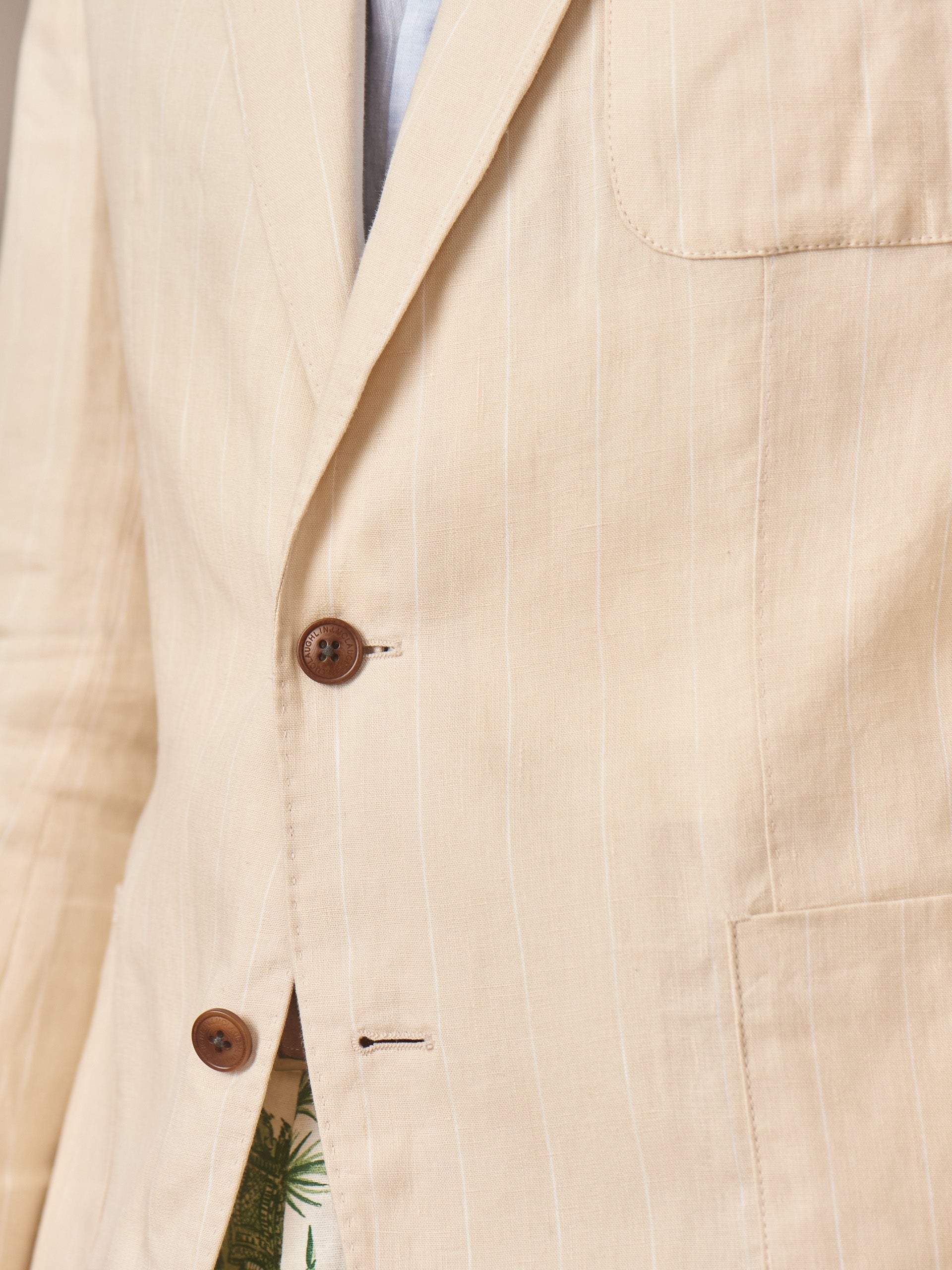 Close-up of J.McLaughlin Brera Linen Sport Coat in Pinstripe featuring lightweight beige linen with subtle vertical stripes and wooden buttons, showcasing effortlessly stylish, enduring designs with innovative fabrics for a legacy of timeless fashion. A destination for defining style. Life, Well-Lived.