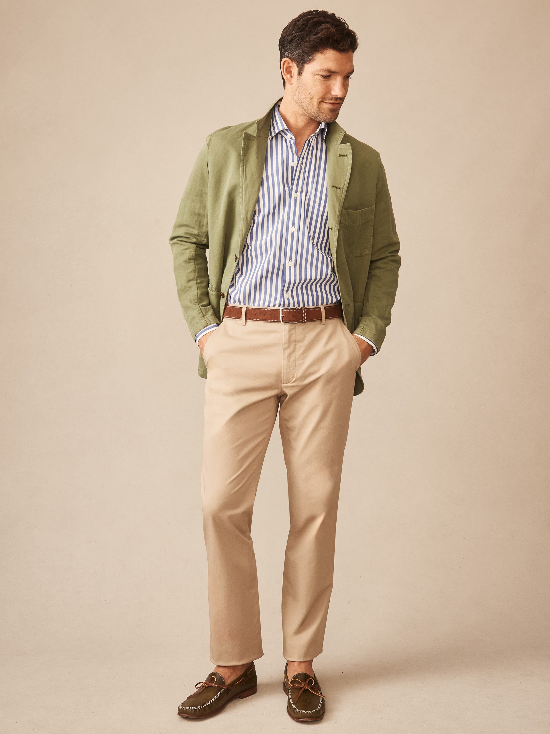 Man wearing khaki Madison Pants paired with a striped shirt, olive green jacket, and brown belt, showcasing J.McLaughlin's effortlessly stylish pants with enduring designs and innovative fabrics.