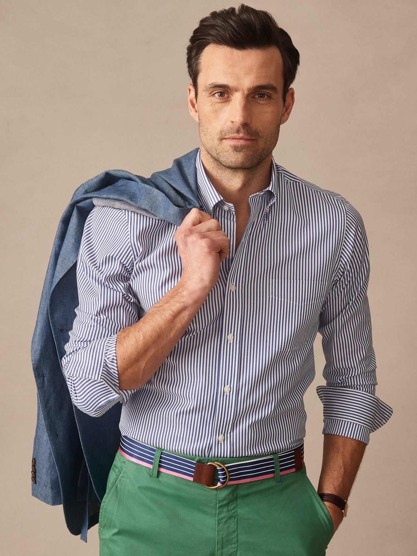 Man wearing a Belvedere Cotton Shirt in Bengal Stripe by J.McLaughlin paired with green pants and a blue jacket draped over his shoulder, showcasing effortlessly stylish, enduring designs in innovative fabrics—a destination for defining style. Life, Well-Lived.