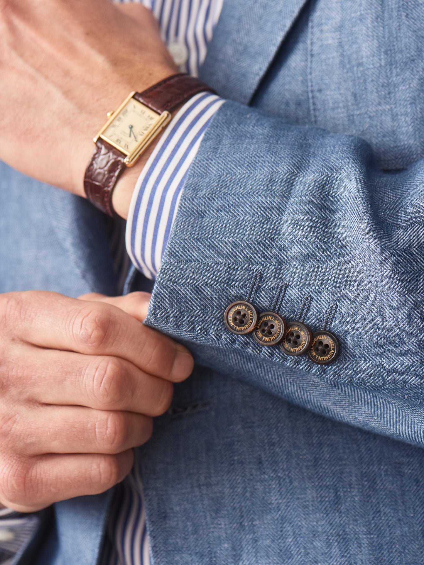 Close-up of a man adjusting the cuff of a blue Brera Linen Sport Coat in Herringbone by J.McLaughlin, showcasing effortlessly stylish design, innovative fabrics, and timeless craftsmanship for enduring style.