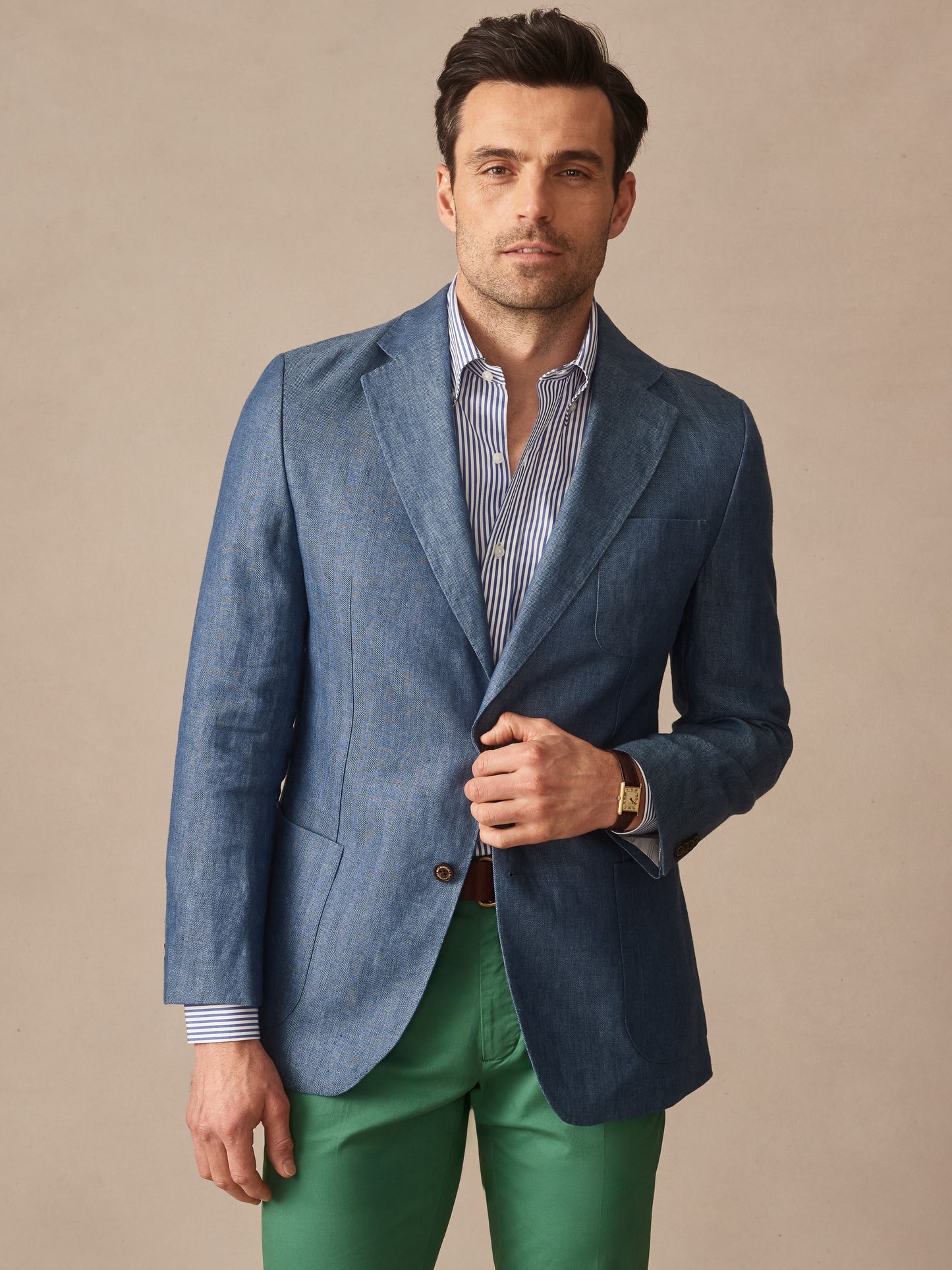 Man wearing a Brera Linen Sport Coat in Herringbone by J.McLaughlin in a sophisticated blue tone paired with a striped shirt and green pants, embodying effortlessly stylish, enduring designs and innovative fabrics. A destination for defining style. Life, Well-Lived.