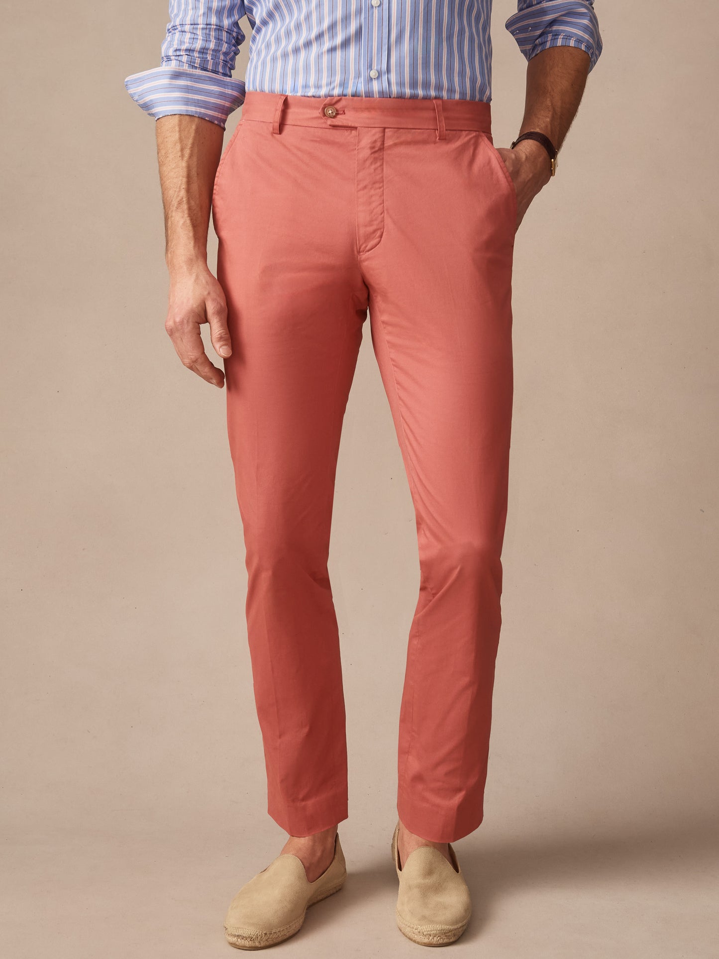 Man wearing coral Madison Pants by J.McLaughlin paired with a striped blue and white shirt and beige slip-on shoes, showcasing effortlessly stylish, enduring designs and innovative fabrics.