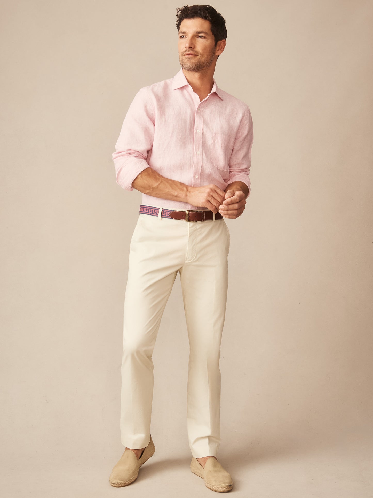 Man wearing light pink button-up shirt paired with cream-colored Madison Pants by J.McLaughlin, styled with a patterned belt and beige slip-on shoes, embodying effortlessly stylish, enduring designs with a legacy of timeless fashion. A destination for defining style. Life, Well-Lived.