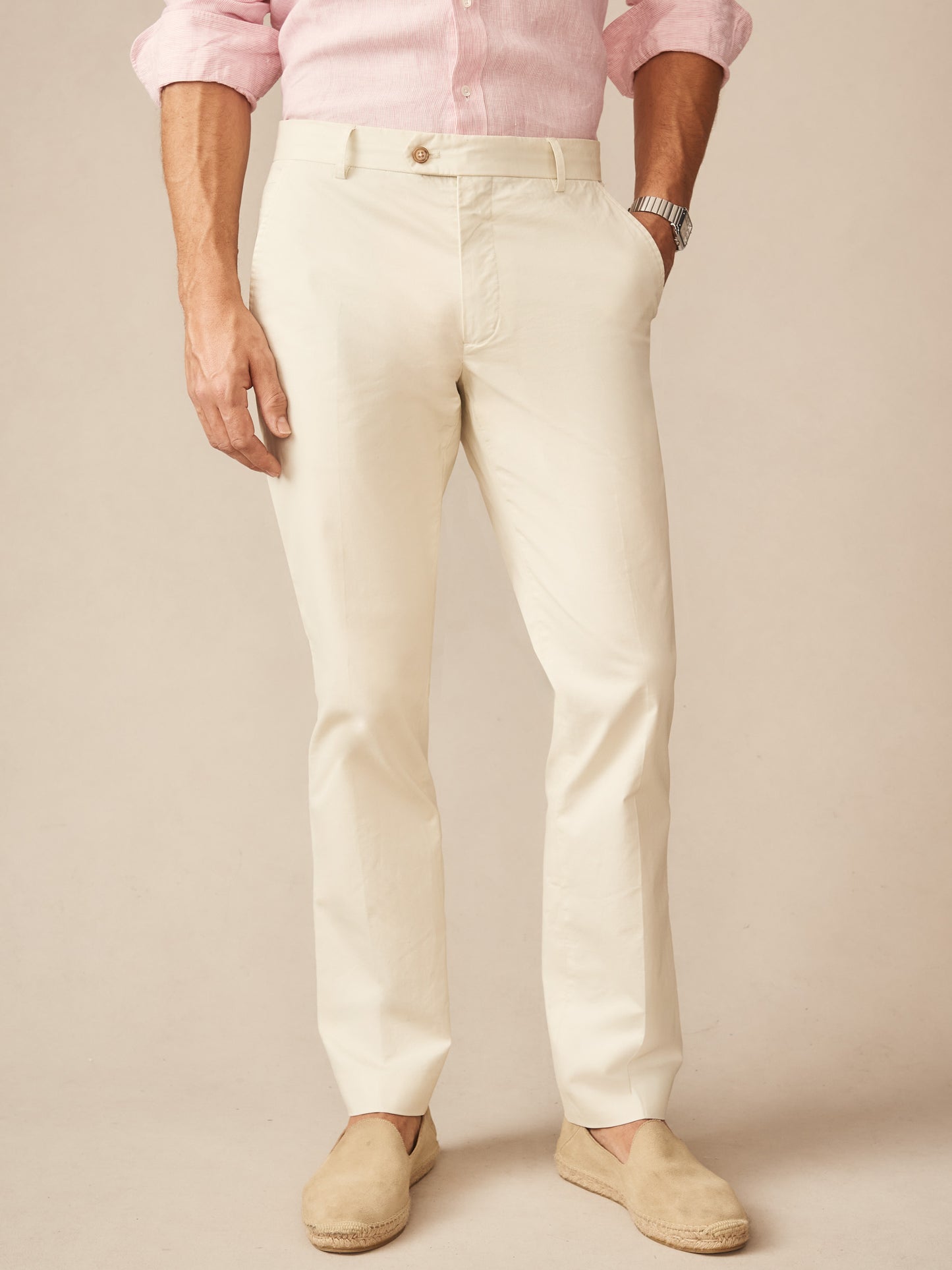Man wearing J. McLaughlin Madison Pants in a light stone color paired with a pale pink shirt and beige slip-on shoes, showcasing effortlessly stylish and enduring designs for defining style.