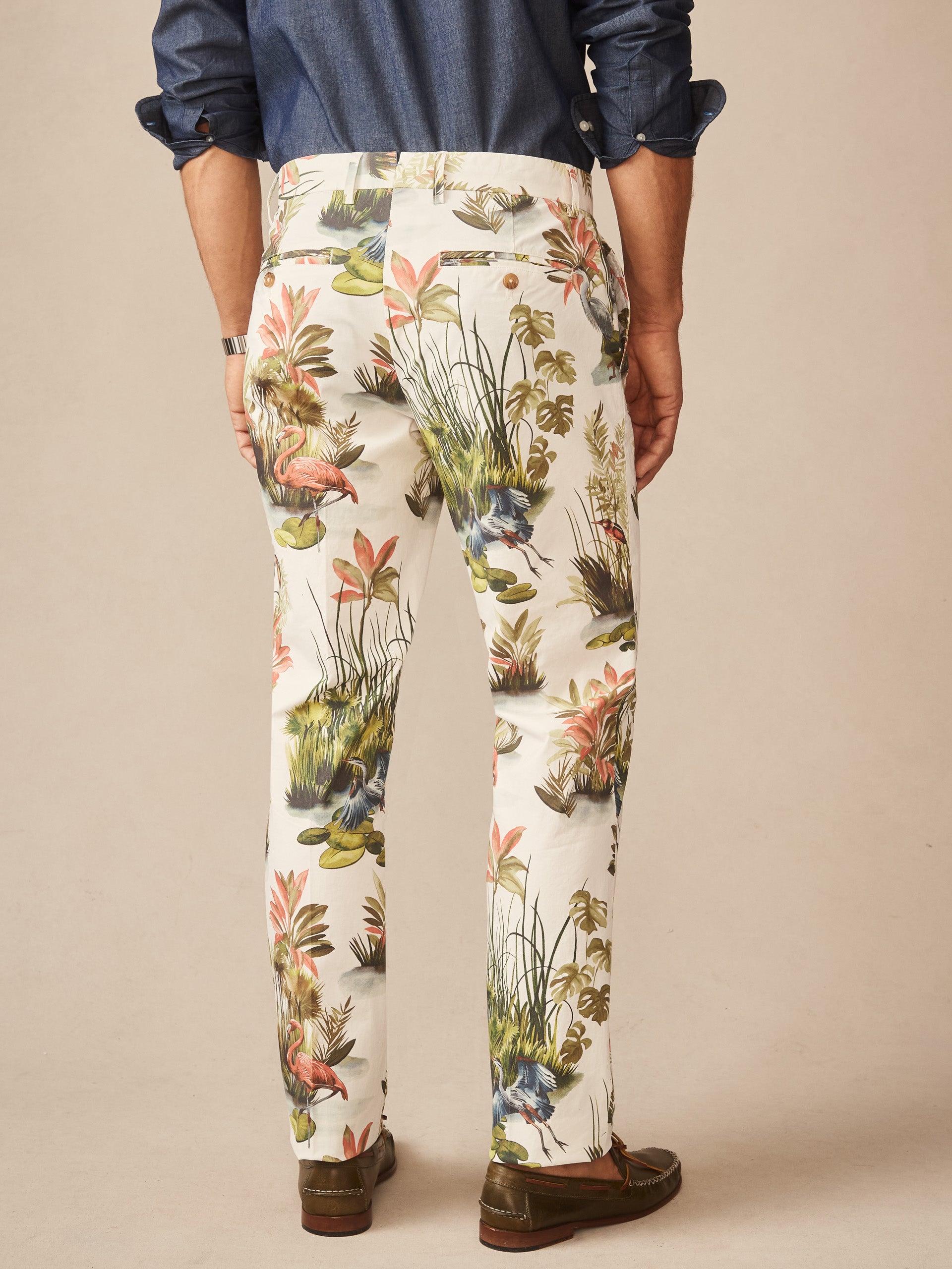 Man wearing Madison Fancy Pants in Tidal Palms by J.McLaughlin featuring a tropical print with flamingos and foliage, paired with a classic blue shirt, showcasing effortlessly stylish, enduring designs and innovative fabrics. A destination for defining style. Life, Well-Lived.