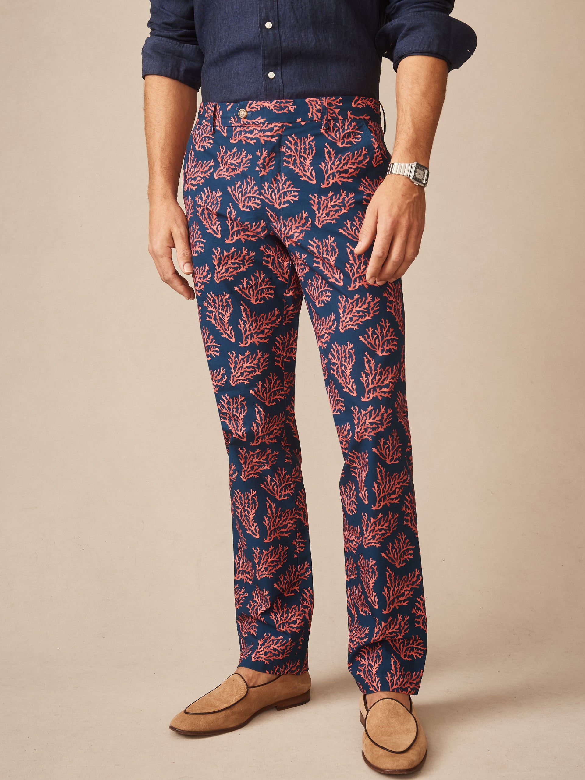 Man wearing Madison Fancy Pants in Midi Coral Cay Texture by J.McLaughlin, featuring an effortlessly stylish coral pattern on navy pants paired with a dark shirt and tan loafers, embodying enduring designs and a legacy of timeless fashion. A destination for defining style. Life, Well-Lived.