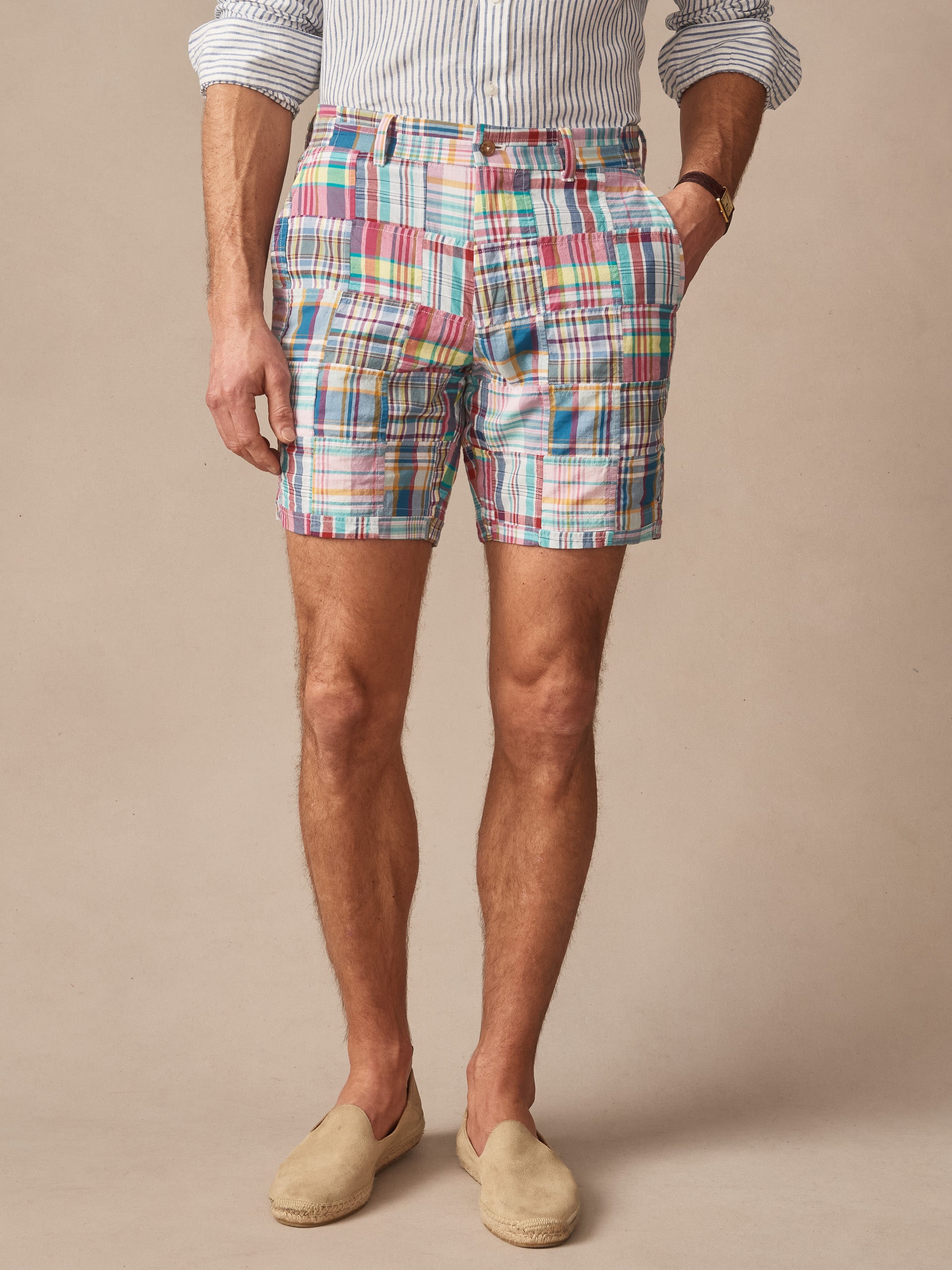 A man wearing J.McLaughlin Chatham Shorts in Patchwork featuring a colorful patchwork design paired with a striped shirt and neutral slip-on shoes, embodying effortlessly stylish, enduring designs and innovative fabrics to uphold a legacy of timeless fashion. A destination for defining style. Life, Well-Lived.