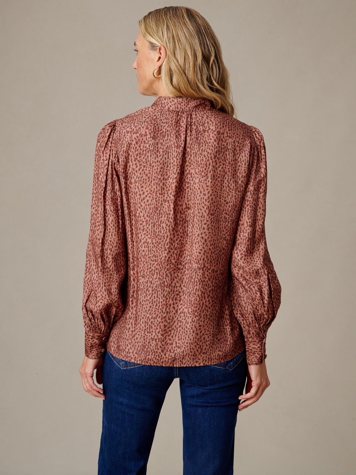 Back view of a woman wearing the Maeve Silk Blend Blouse in Leopardette by J.McLaughlin with raglan sleeves and a stand collar styled with dark blue jeans