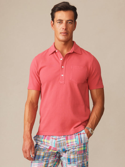 A man modeling a timeless Mantle Pique Polo in red by J.McLaughlin, paired with vibrant plaid shorts, showcasing effortlessly stylish and enduring designs with innovative fabrics.