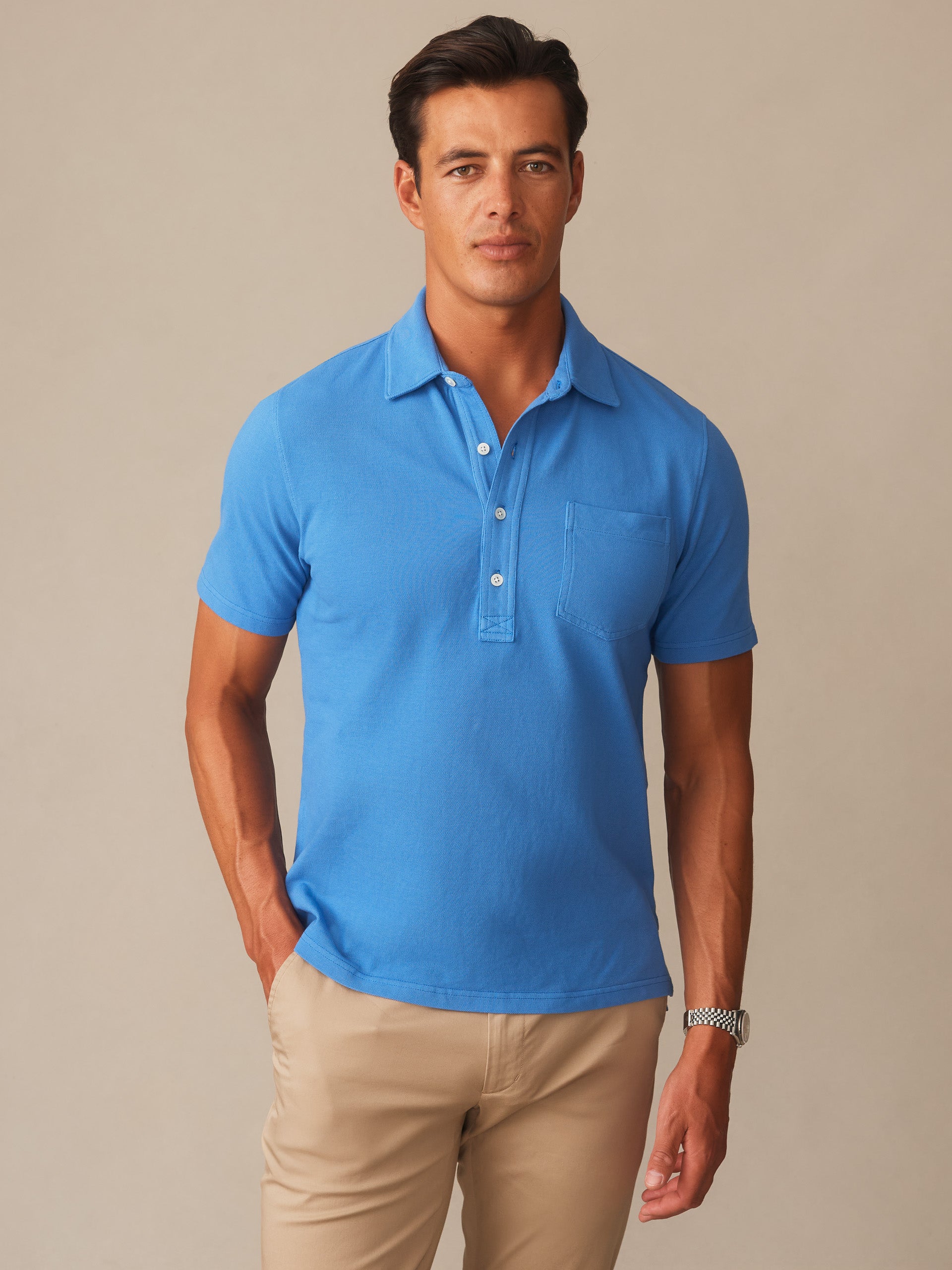 Man wearing a pacific blue Mantle Pique Polo by J.McLaughlin, styled with classic khaki pants, showcasing effortlessly stylish, enduring designs with innovative fabrics.