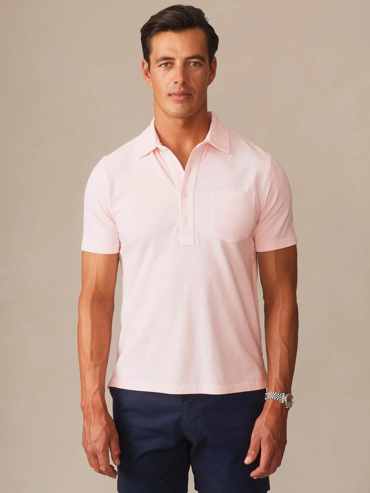 Man wearing a light pink Mantle Pique Polo by J.McLaughlin paired with dark navy pants, showcasing effortlessly stylish and enduring designs for a timeless look.