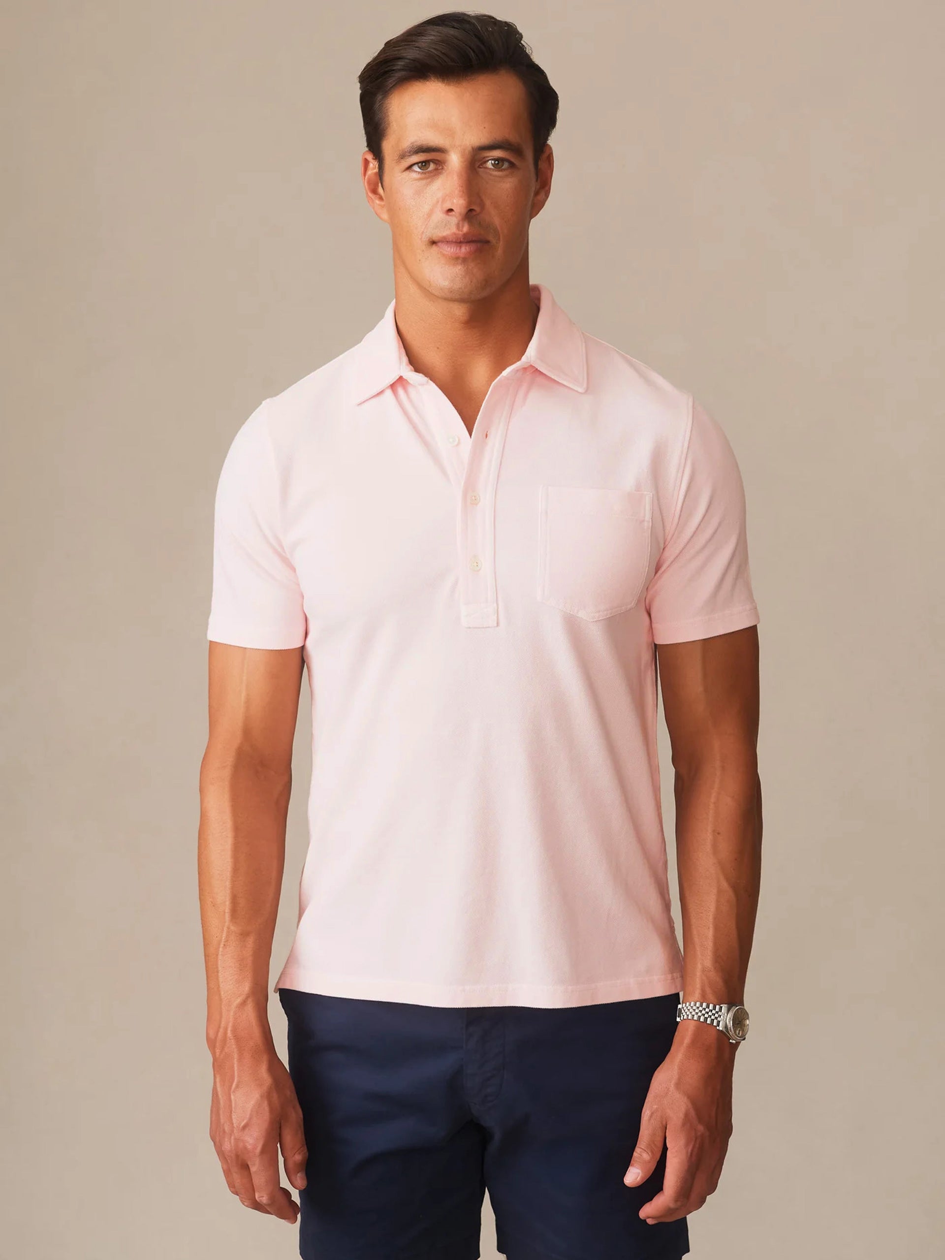 Man wearing a light pink Mantle Pique Polo by J.McLaughlin paired with dark navy pants, showcasing effortlessly stylish and enduring designs for a timeless look.