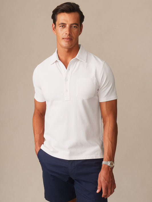 Man wearing a white Mantle Pique Polo by J.McLaughlin paired with navy shorts, showcasing effortlessly stylish and enduring designs crafted with innovative fabrics for a legacy of timeless fashion.