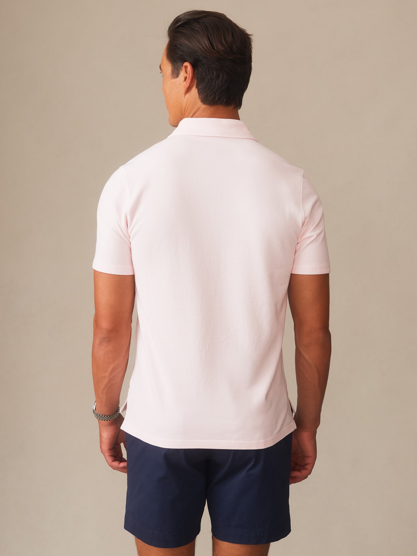Man wearing a light pink Mantle Pique Polo by J.McLaughlin, paired with navy shorts, showcasing effortlessly stylish, enduring designs with a legacy of timeless fashion.