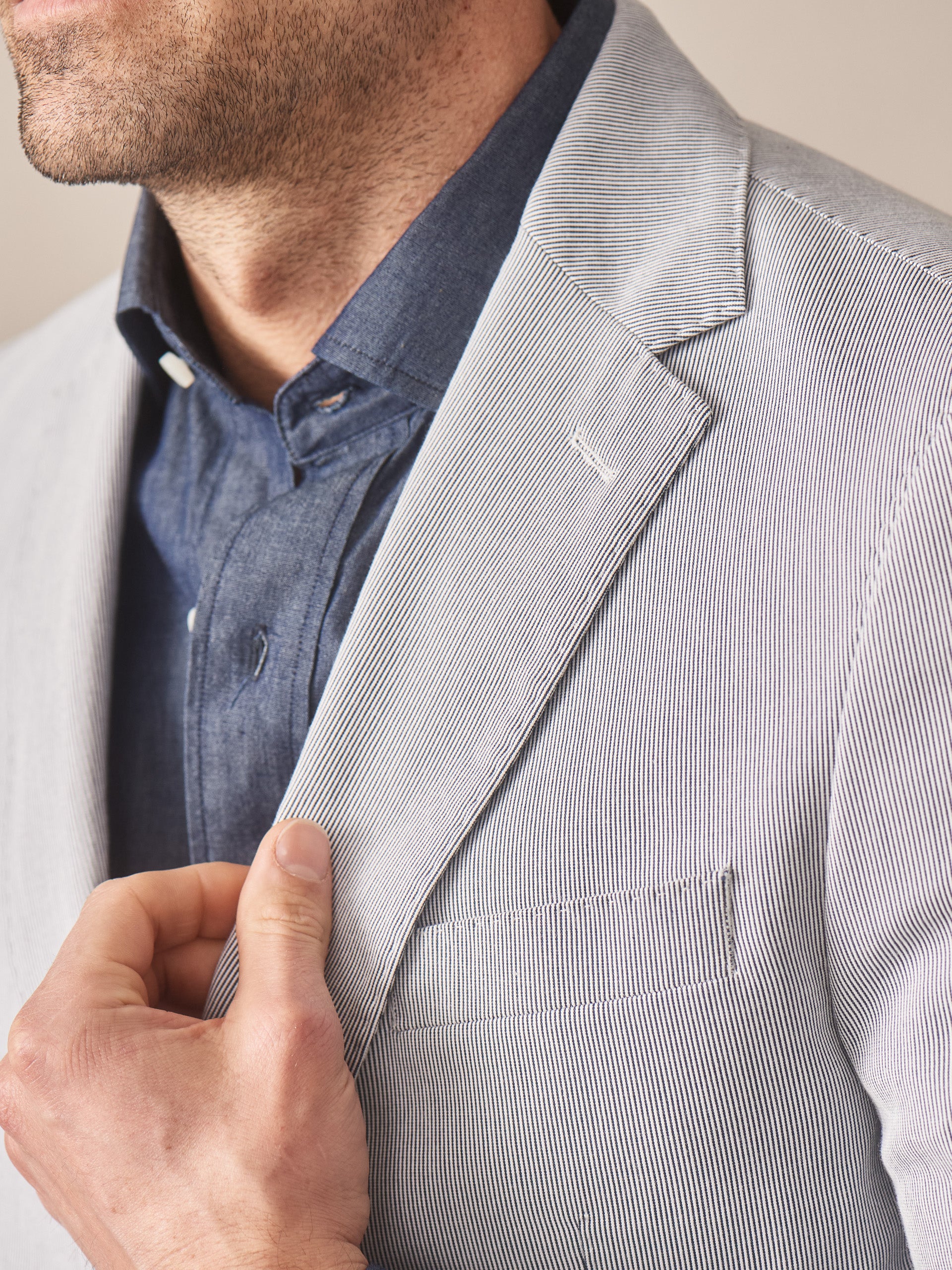 Close-up of a man wearing a J.McLaughlin Suffolk Sport Coat in Fineline over a dark blue shirt, showcasing the classic, fine striped fabric and tailored craftsmanship.
