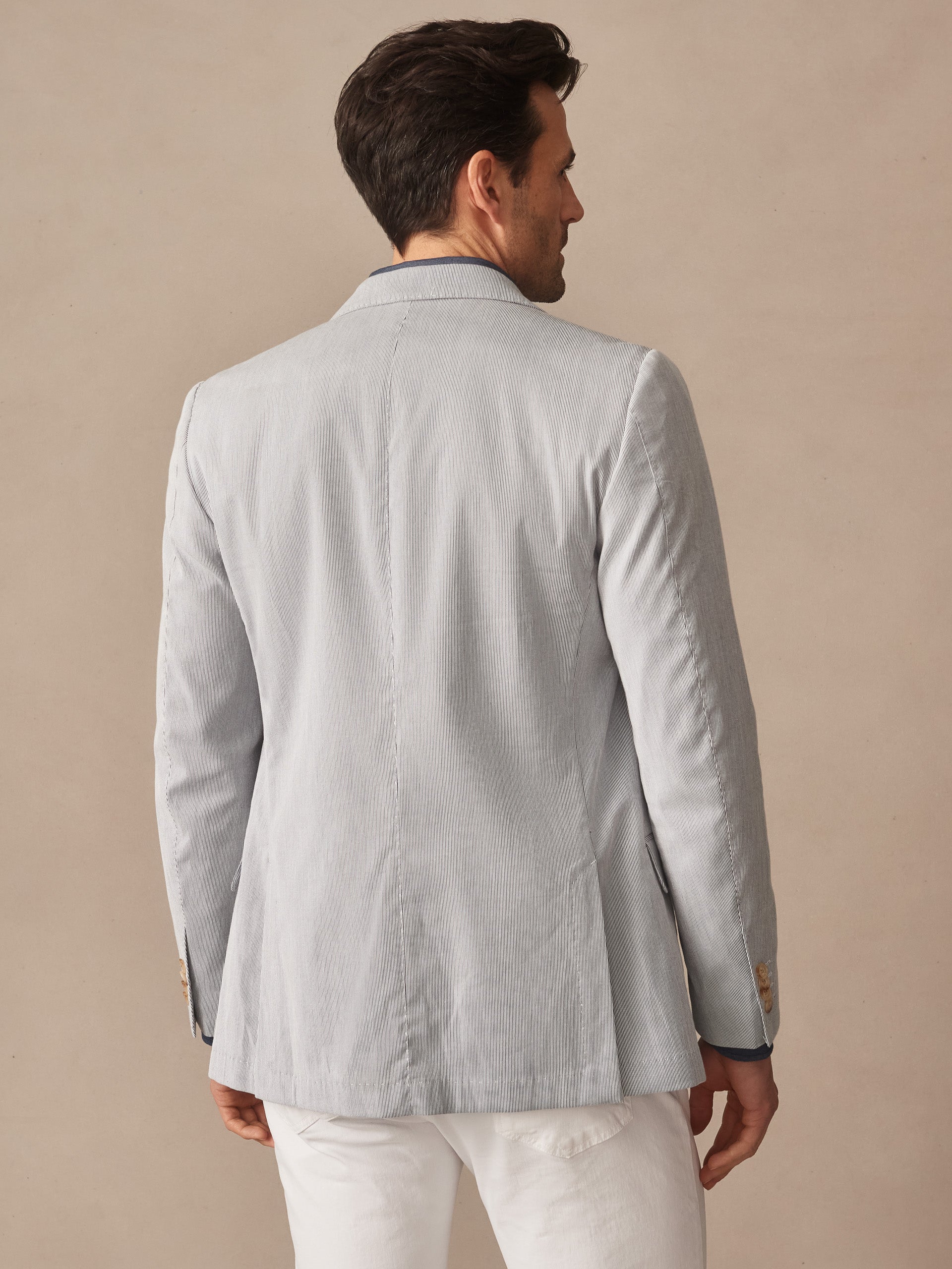 Man seen from the back wearing a J. McLaughlin Suffolk Sport Coat in Fineline, a light textured jacket designed with classic, timeless style paired with white pants.