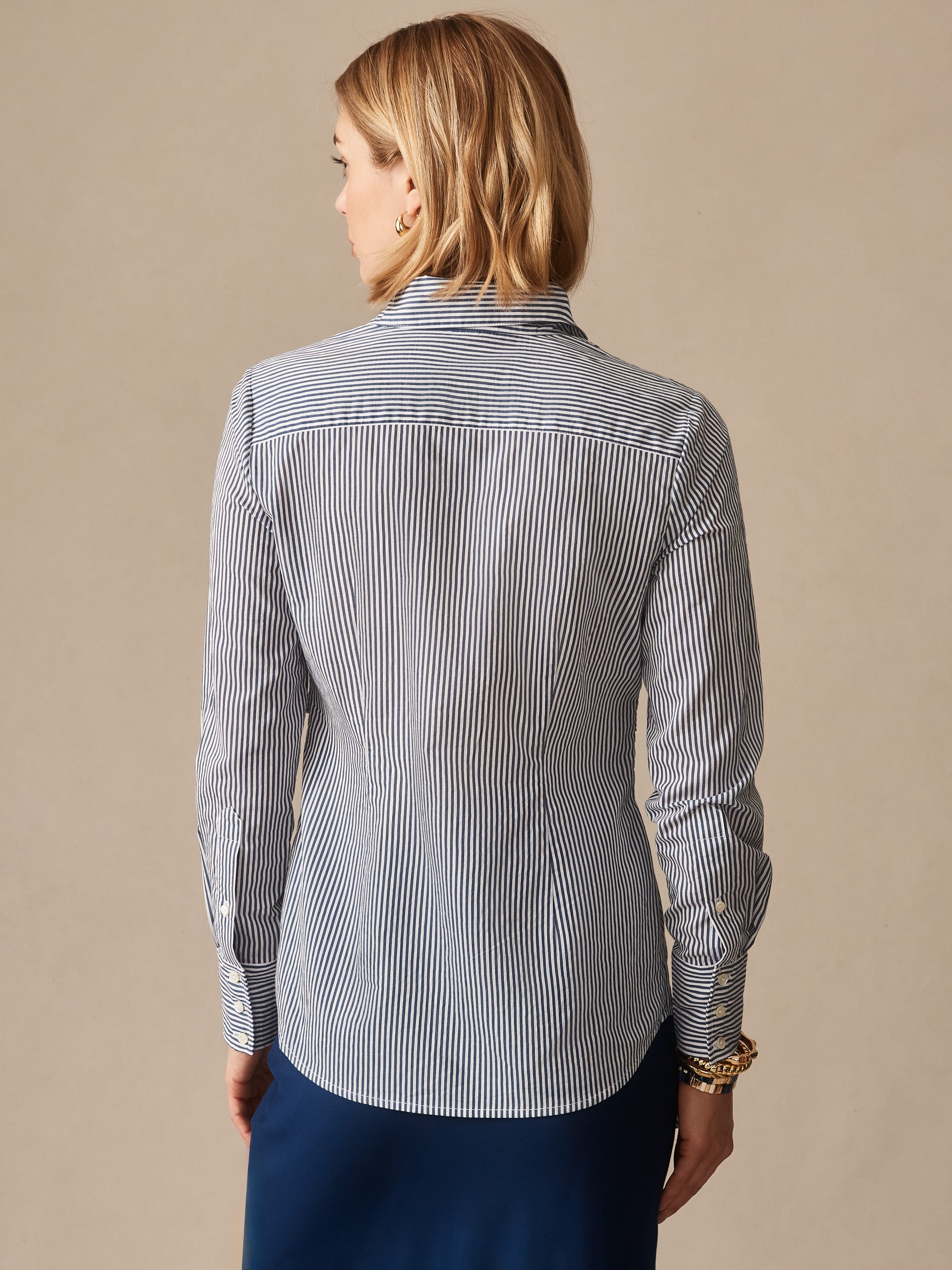 A rear view of a woman wearing the Margaux Shirt in Stripe by J.McLaughlin, featuring effortlessly stylish blue and white vertical stripes, embodying enduring designs and a legacy of timeless fashion. A destination for defining style. Life, Well-Lived.