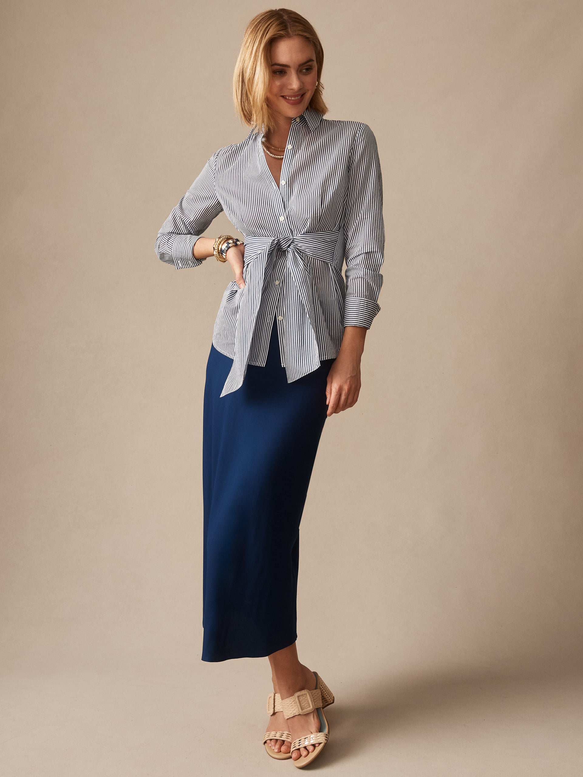Woman wearing the Margaux Shirt in Stripe by J.McLaughlin, styled with a navy skirt and beige sandals, showcasing effortlessly stylish, enduring designs and innovative fabrics for a legacy of timeless fashion. A destination for defining style. Life, Well-Lived.