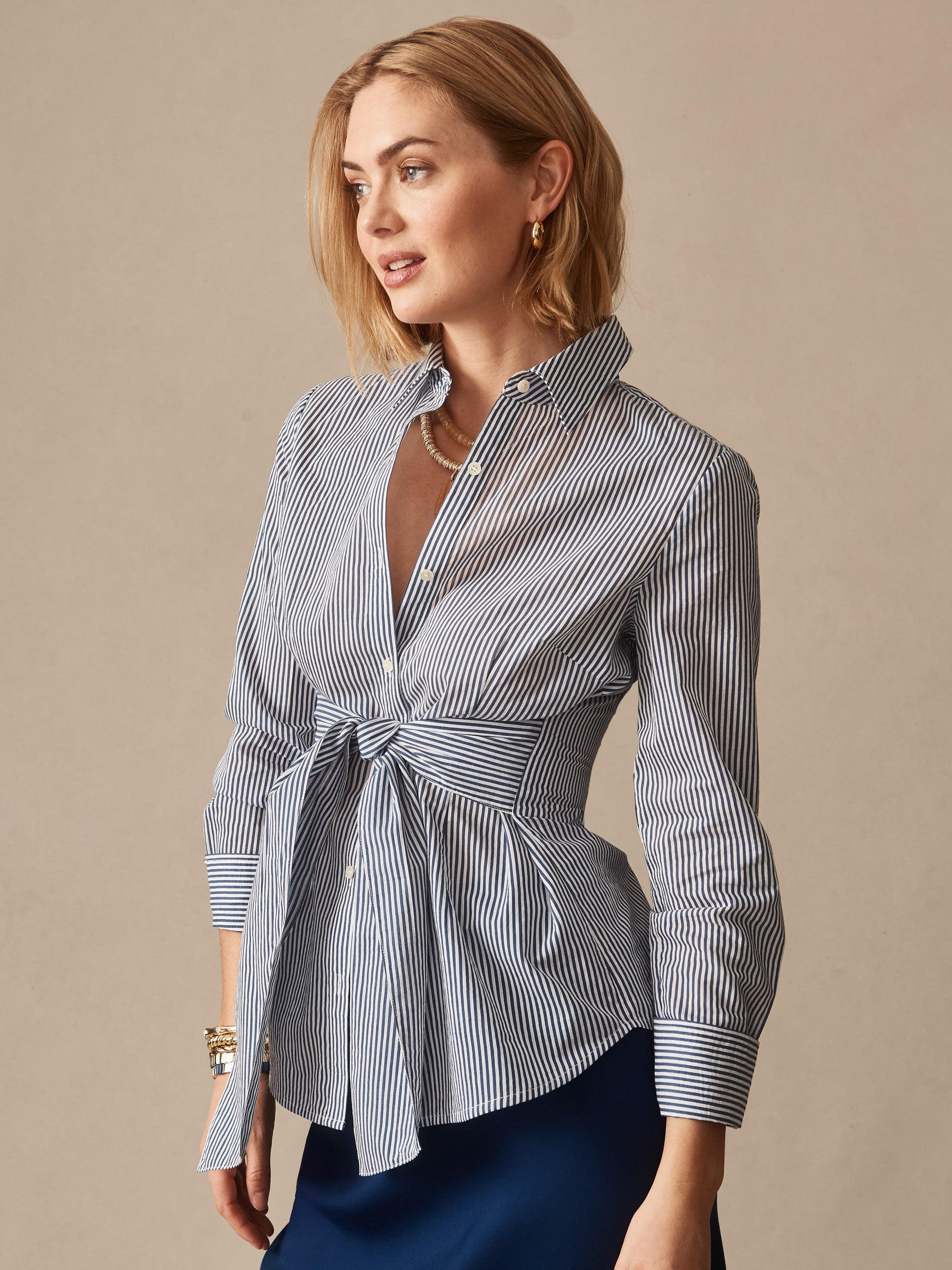 Woman wearing the Margaux Shirt in Stripe by J.McLaughlin, featuring classic navy and white stripes with a stylish waist tie, epitomizing effortlessly stylish, enduring designs and a legacy of timeless fashion from a destination for defining style. Life, Well-Lived.