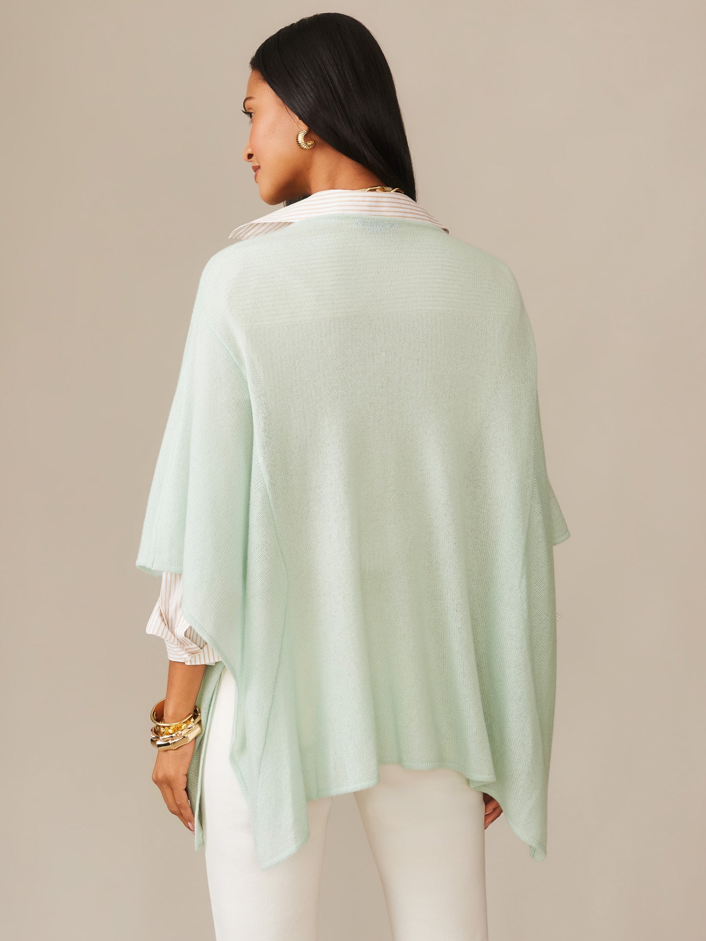 A woman seen from behind wearing the Marin Cashmere Poncho in soft mint, paired with white pants and gold jewelry, showcasing J.McLaughlin’s effortlessly stylish, enduring design.