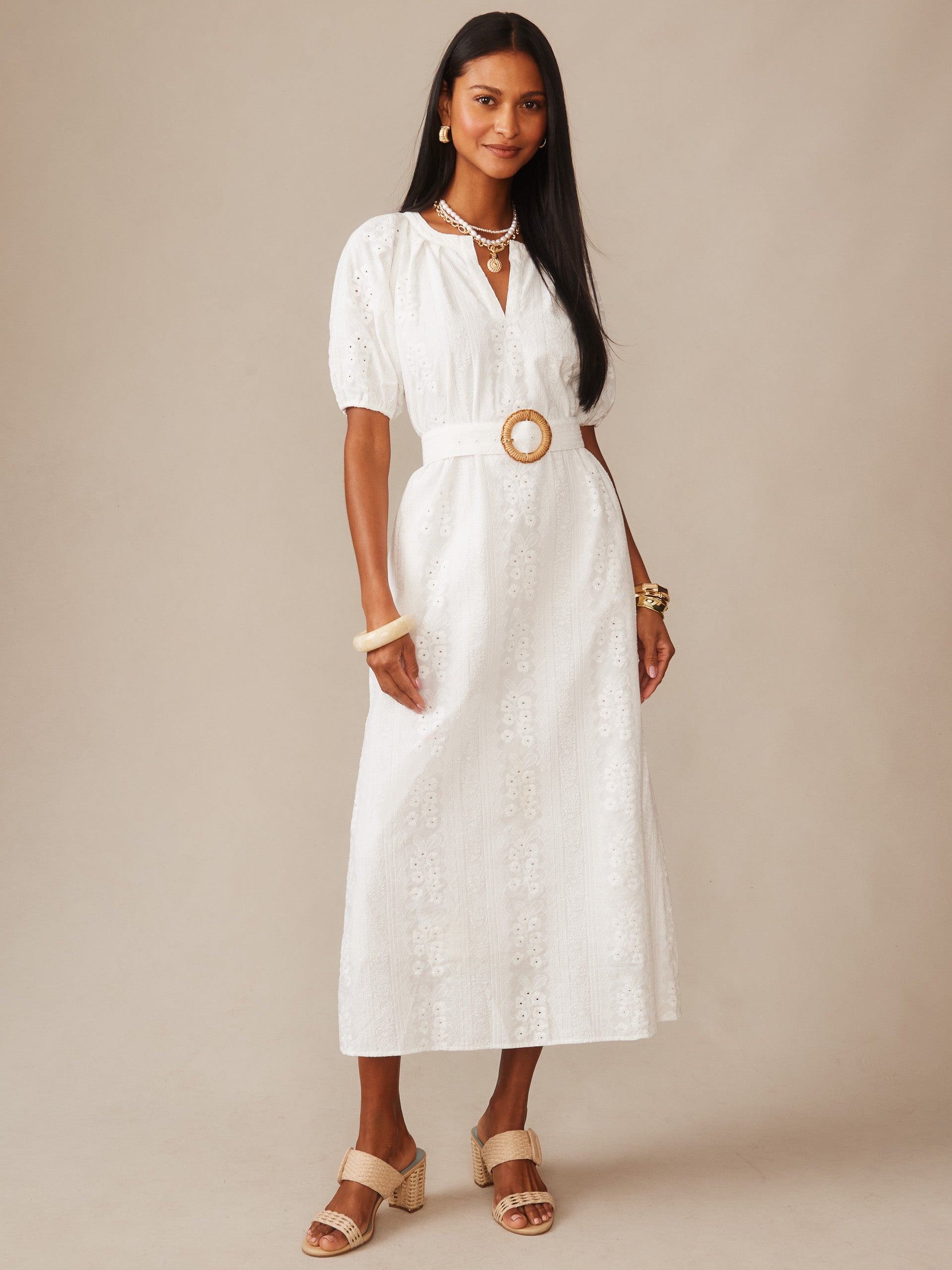 A model wearing the Marley Eyelet Dress by J.McLaughlin, featuring elegant white eyelet fabric with puff sleeves and a waist belt, embodying effortlessly stylish, enduring designs and innovative fabrics.
