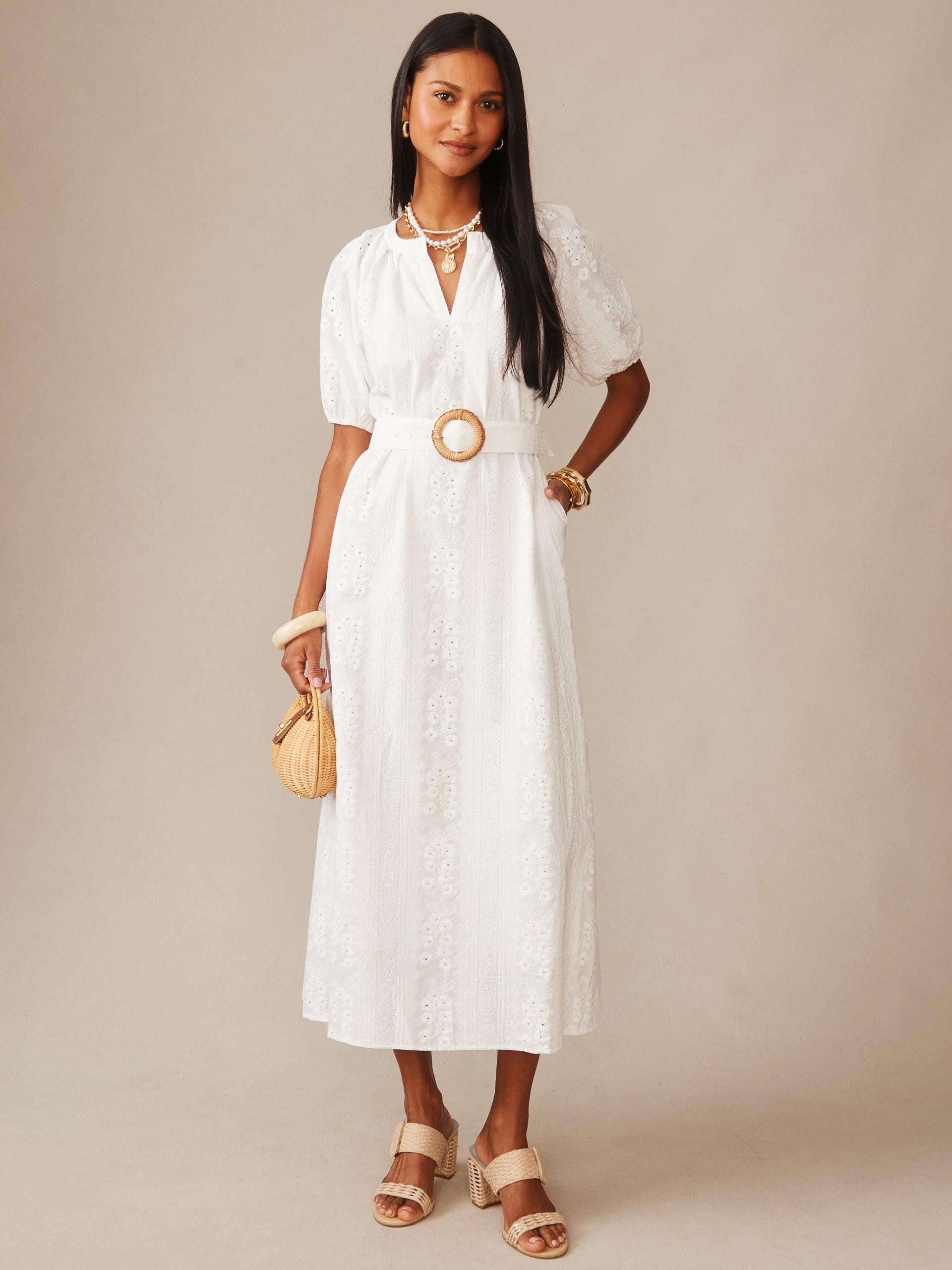 A woman wearing a white Marley Eyelet Dress by J.McLaughlin featuring delicate eyelet embroidery, puff sleeves, and a belted waist, styled with minimal jewelry and neutral sandals, embodying effortlessly stylish, enduring designs with a legacy of timeless fashion.