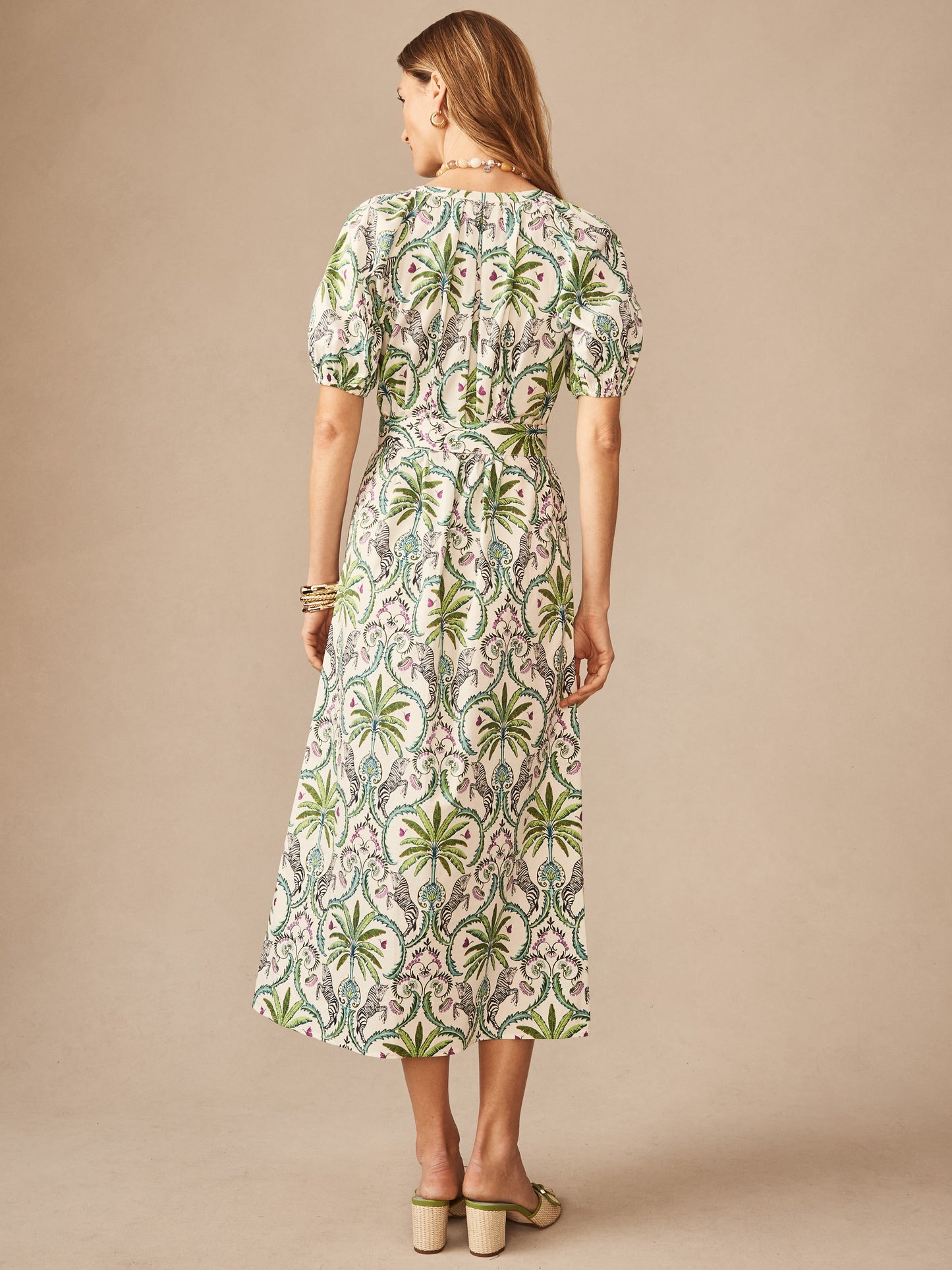 Woman wearing the Marley Dress in Zebra Isle by J.McLaughlin, featuring a green and off-white botanical print, short puff sleeves, and a midi length, showcasing effortlessly stylish and enduring designs in a legacy of timeless fashion. A destination for defining style. Life, Well-Lived.
