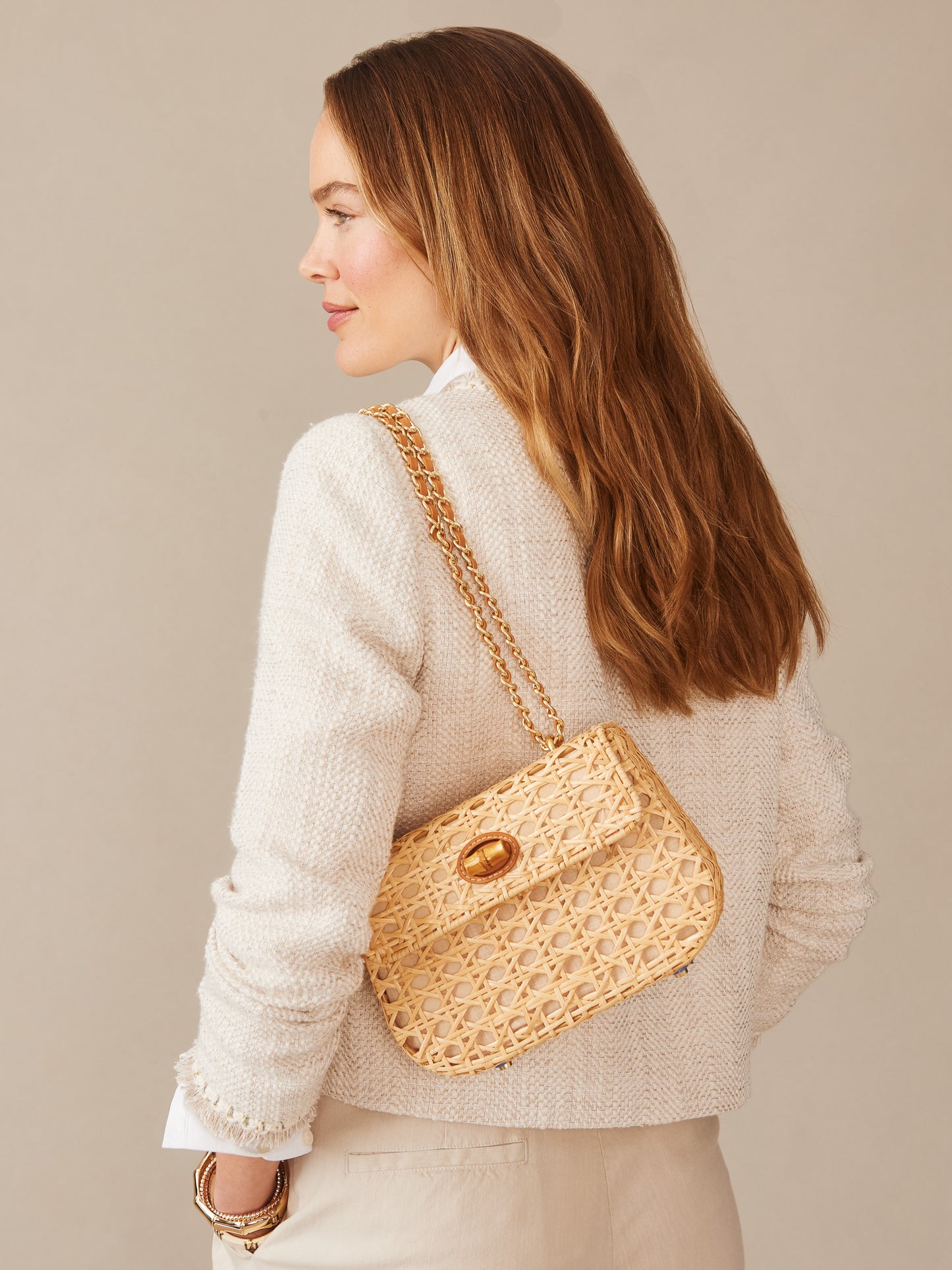 A woman models the Waverly Wicker Handbag by J.McLaughlin, featuring a woven wicker design and gold chain strap, embodying effortlessly stylish, enduring designs for a life well-lived.