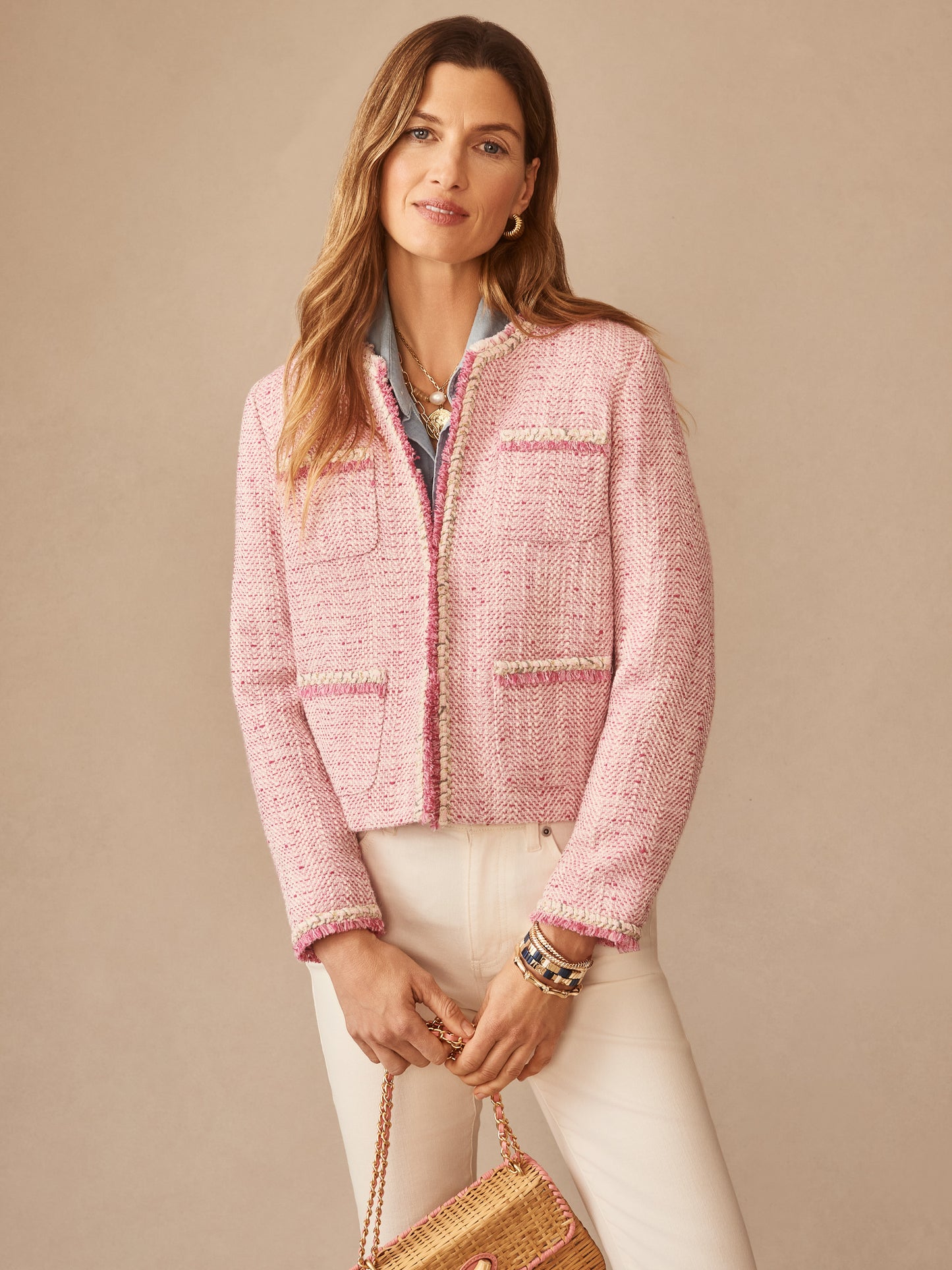 Woman wearing a pink Martha Bouclé Jacket by J.McLaughlin, paired with white pants and a woven bag, showcasing effortlessly stylish, enduring designs and a legacy of timeless fashion.