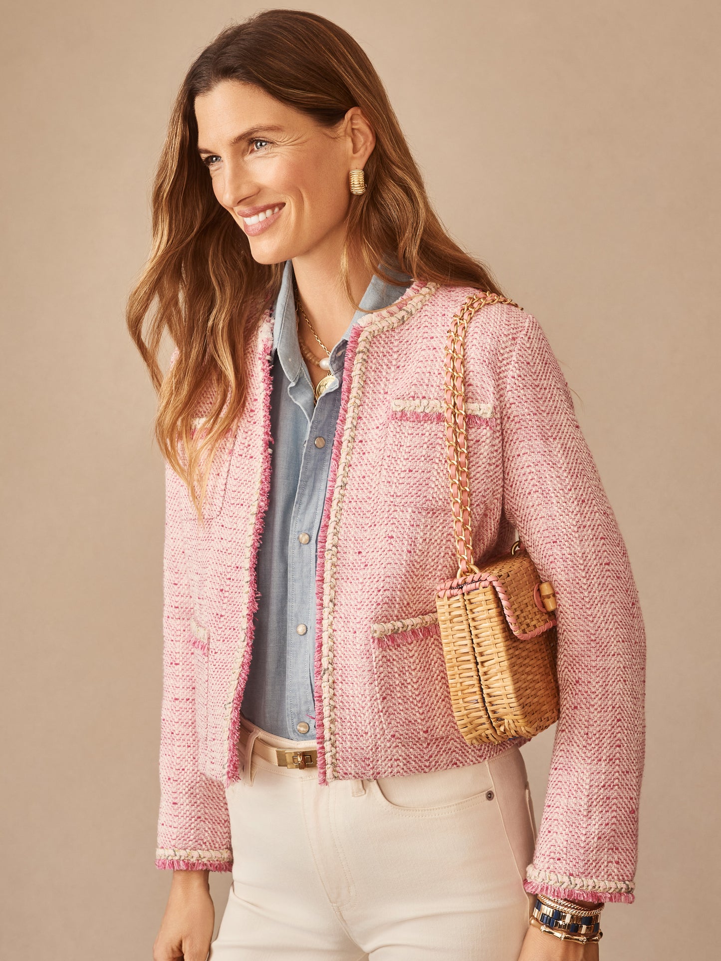 A smiling woman models the Martha Bouclé Jacket by J.McLaughlin in soft pink, paired with a chambray shirt and woven bag, showcasing effortlessly stylish, enduring designs with a legacy of timeless fashion. A destination for defining style. Life, Well-Lived.