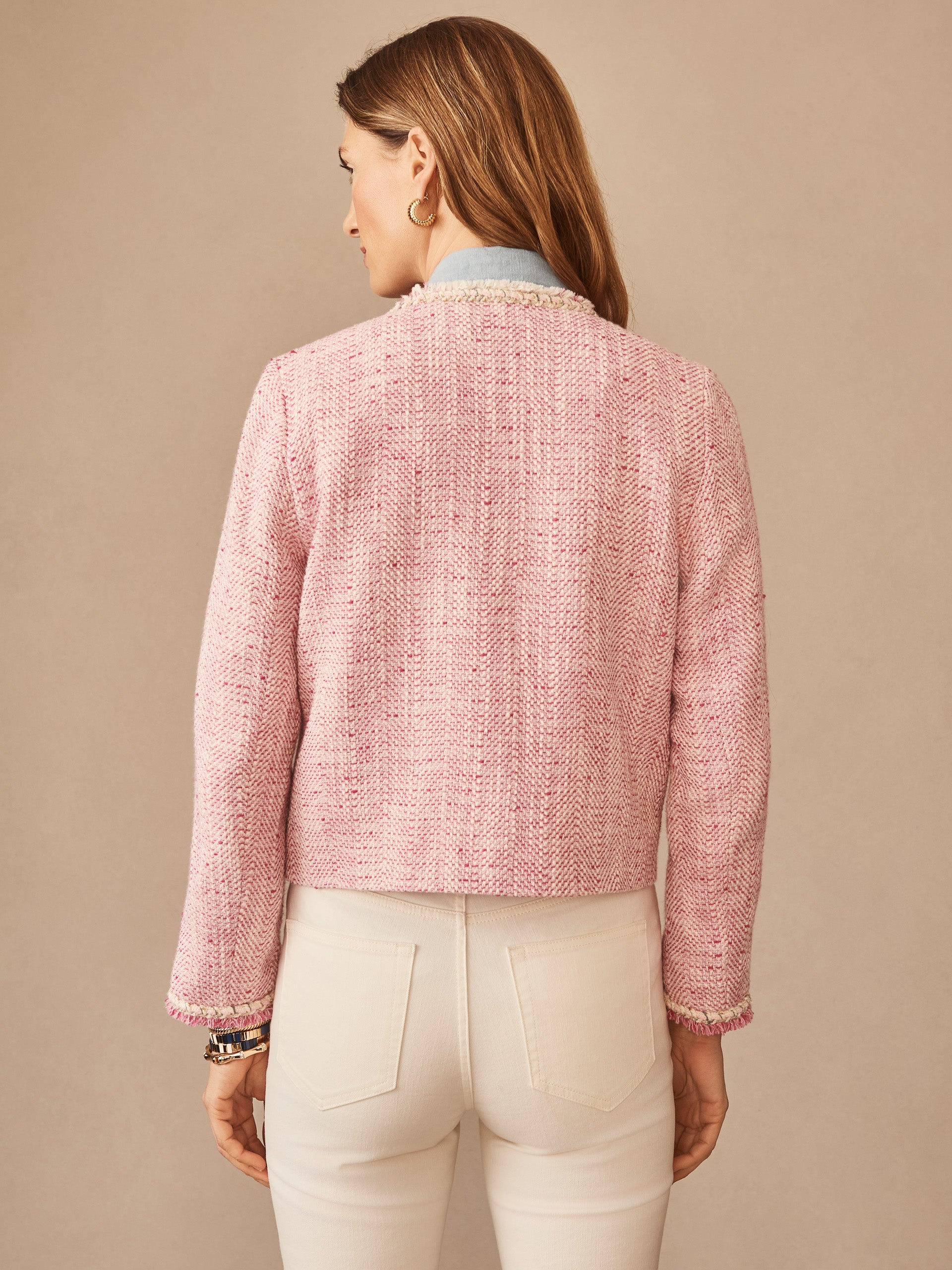 A woman seen from behind wearing a pink textured Martha Bouclé Jacket by J.McLaughlin paired with white pants, showcasing effortlessly stylish design and enduring appeal.