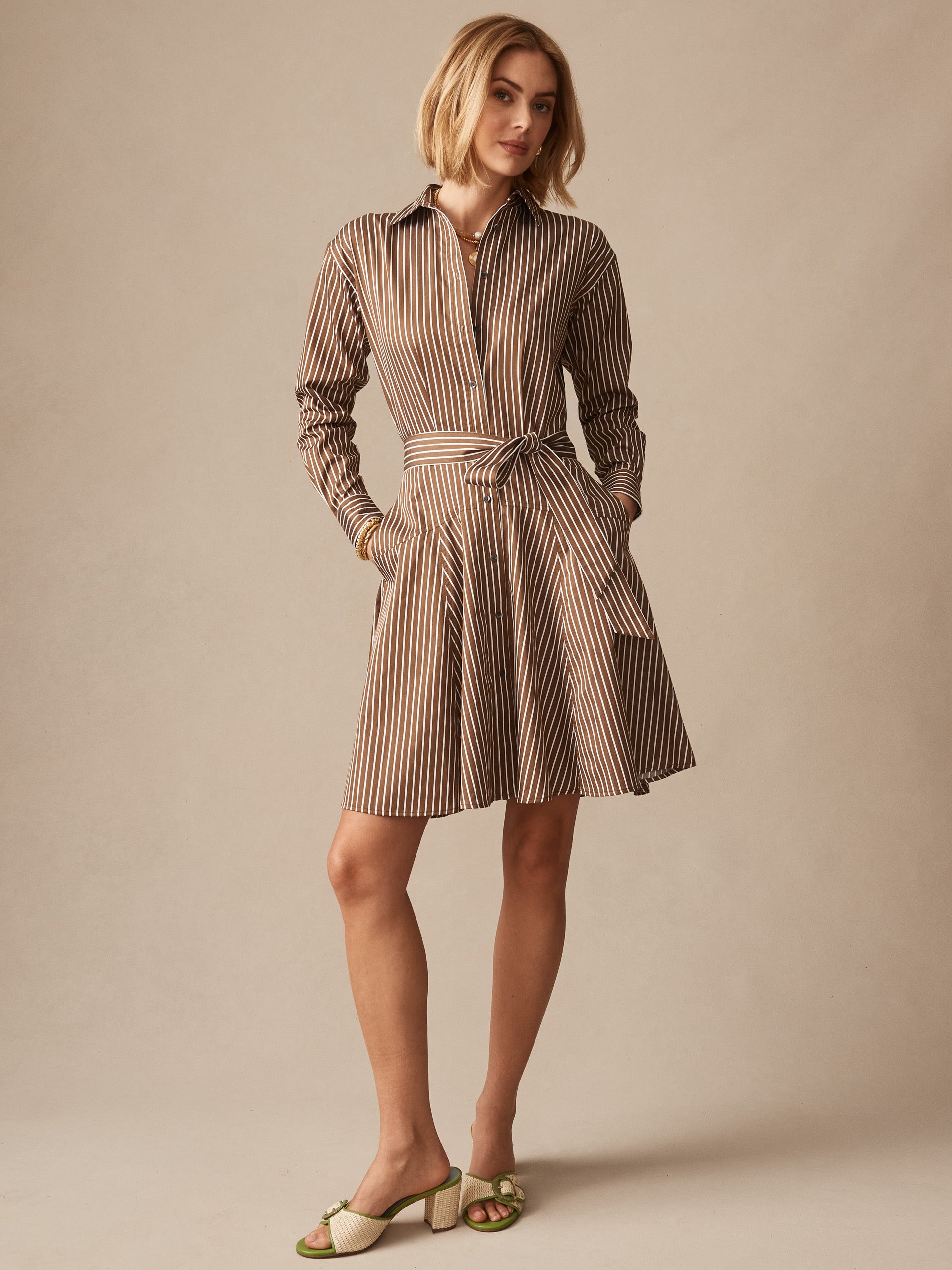 Woman wearing a brown and white striped Mary Dress in Stripe by J.McLaughlin, featuring a tie waist and classic shirt collar, epitomizing effortlessly stylish, enduring designs.