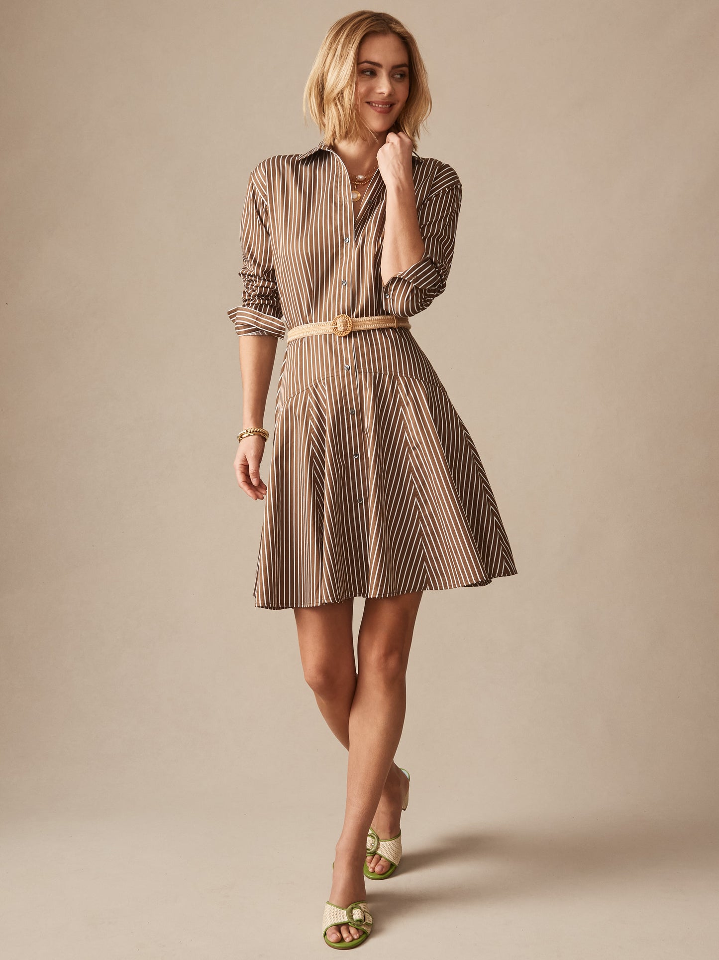 A woman models the Mary Dress in Stripe by J.McLaughlin featuring a brown and white striped pattern, a belted waist, and a button-down shirt style, showcasing effortlessly stylish, enduring designs crafted for a life well-lived.