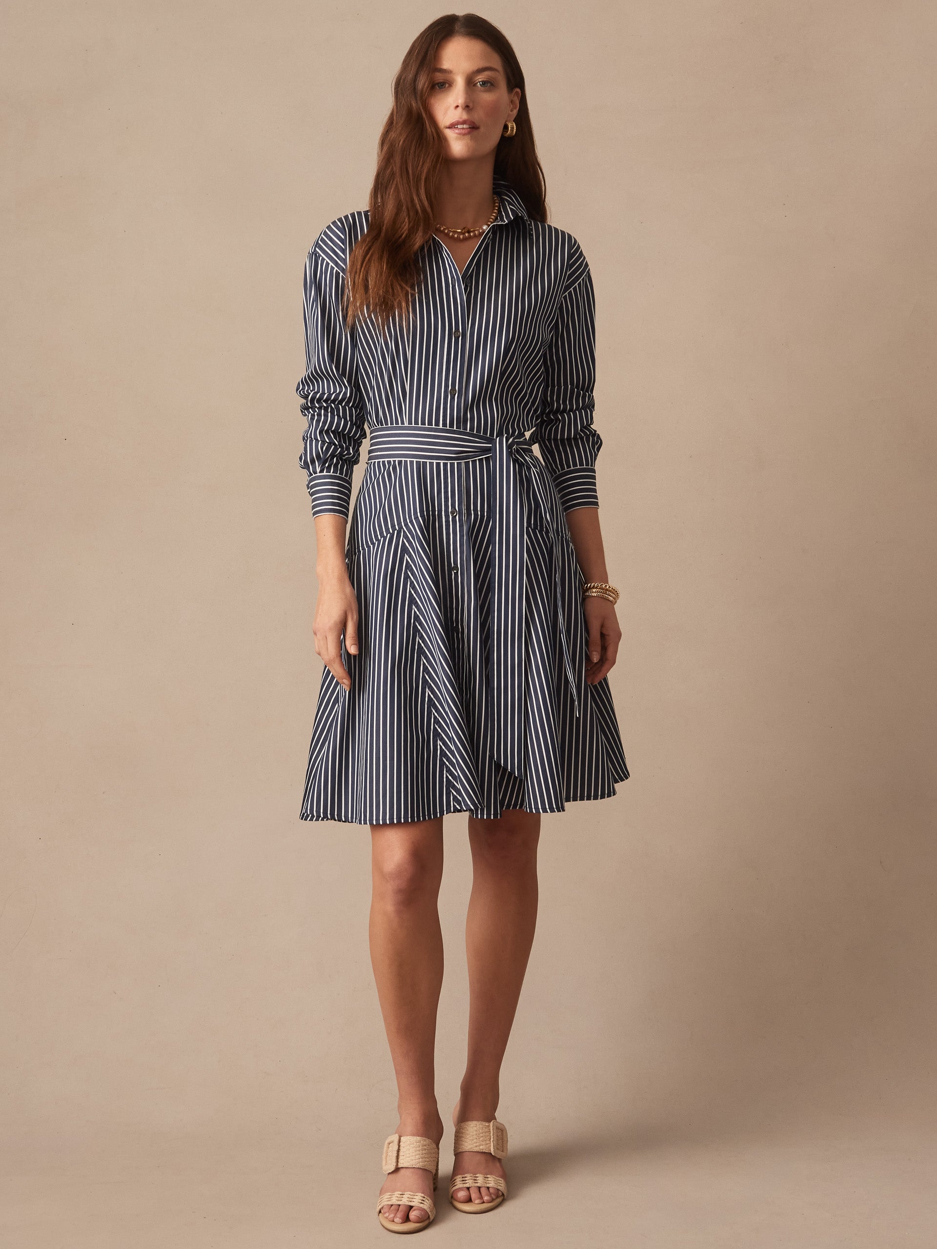 Woman wearing a navy and white striped Mary Dress in Stripe by J.McLaughlin, featuring a button-down front and a self-tie belt, showcasing effortlessly stylish, enduring designs.