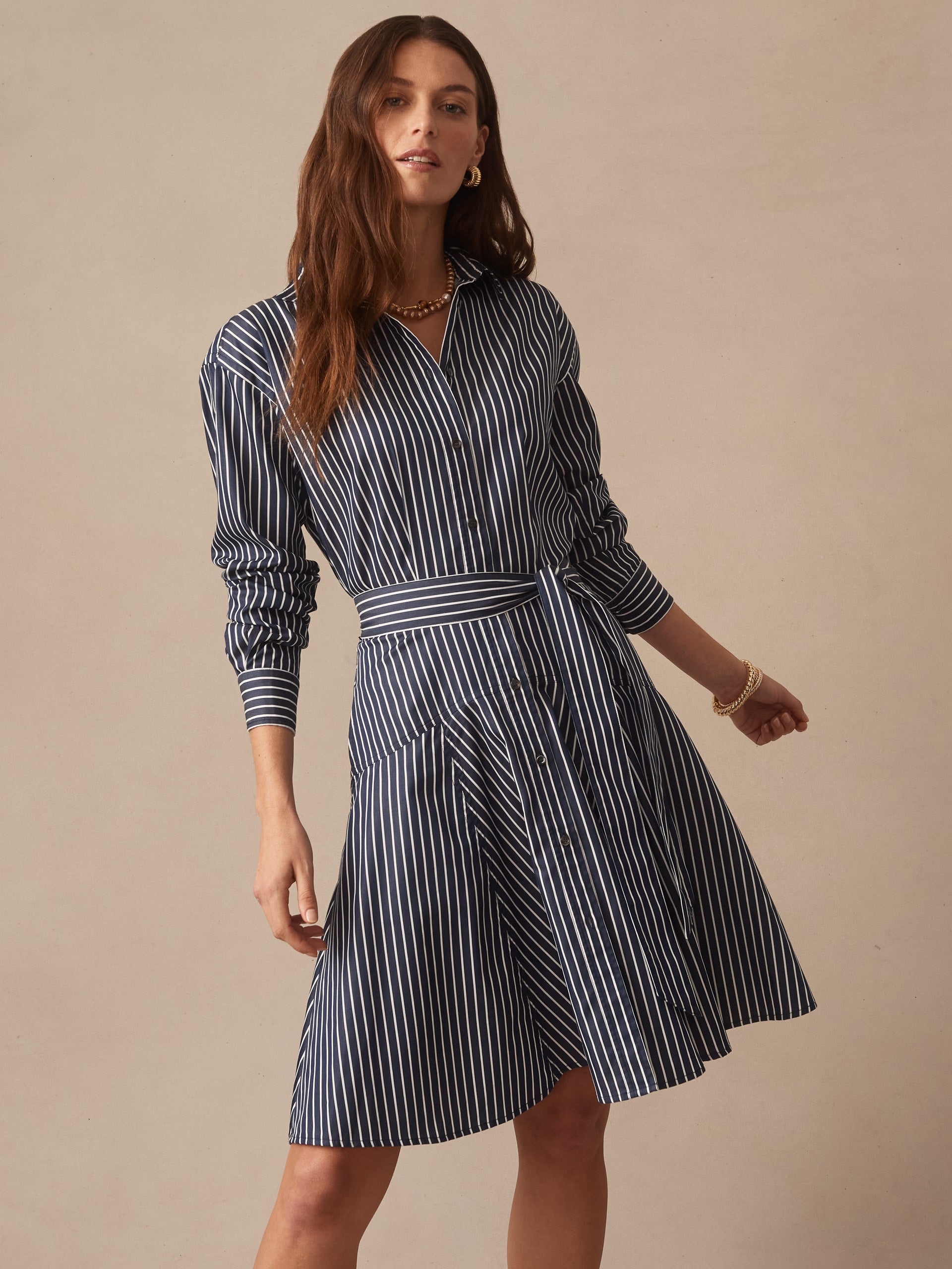 Woman wearing a navy and white striped Mary Dress in Stripe by J.McLaughlin, featuring a belted waist and long sleeves, showcasing effortlessly stylish, enduring designs in innovative fabrics.