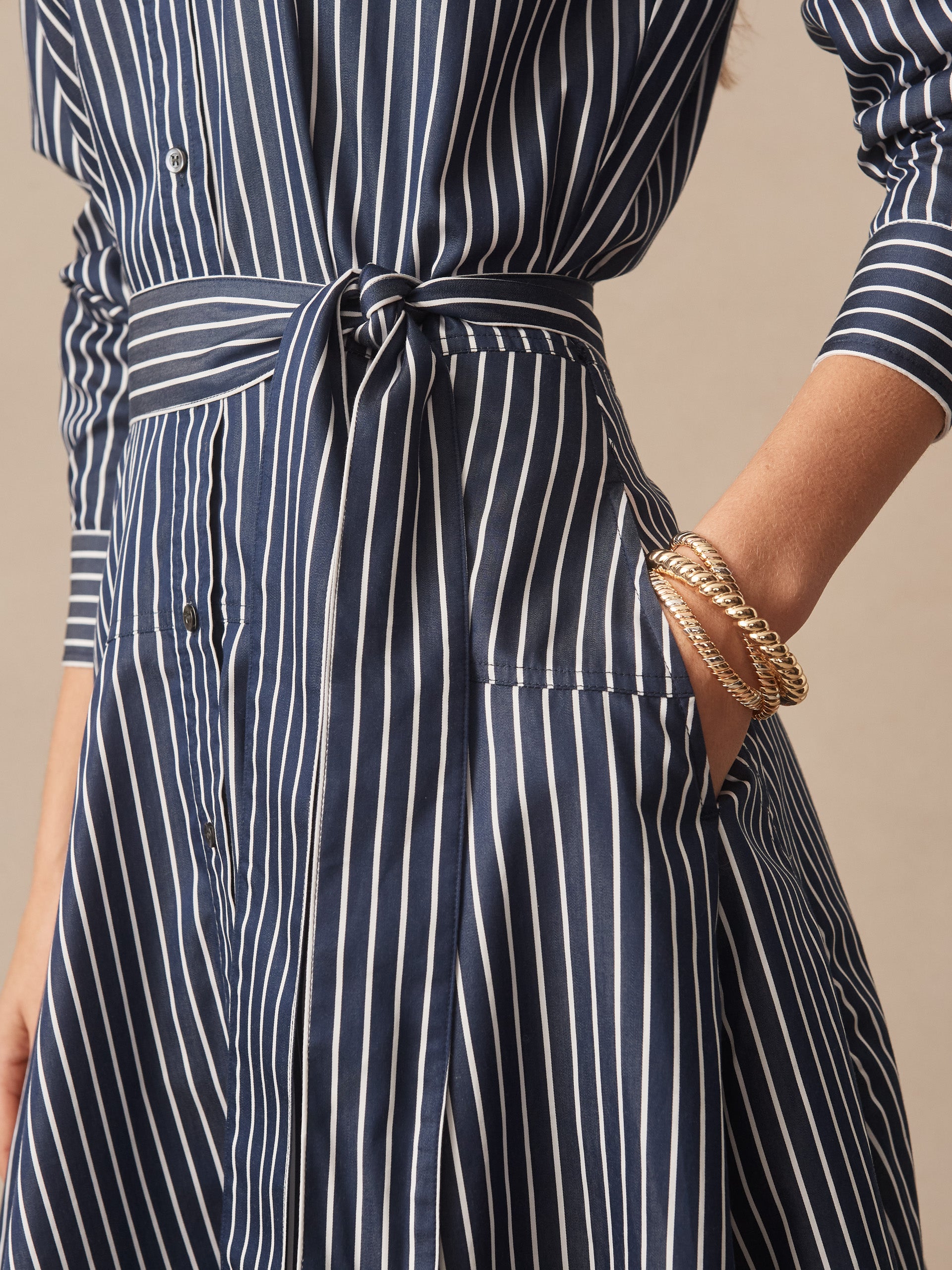 Close-up of a navy and white striped Mary Dress in Stripe by J.McLaughlin featuring a tied waist belt and gold bracelets, showcasing effortlessly stylish, enduring designs with a legacy of timeless fashion—A destination for defining style. Life, Well-Lived.