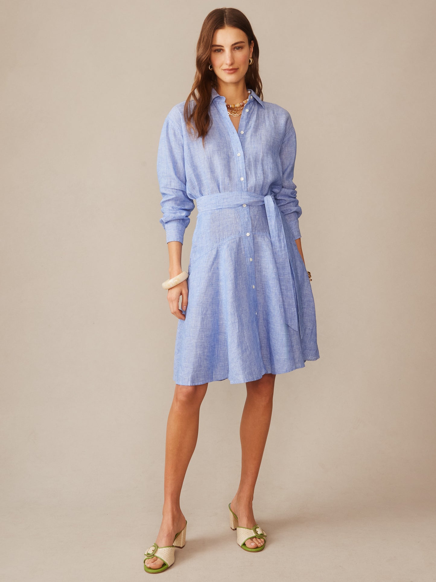 Woman wearing a blue button-down Mary Linen Dress in Stripe by J.McLaughlin, styled with layered necklaces, a bracelet, and green heeled sandals, showcasing effortlessly stylish, enduring designs and innovative fabrics.