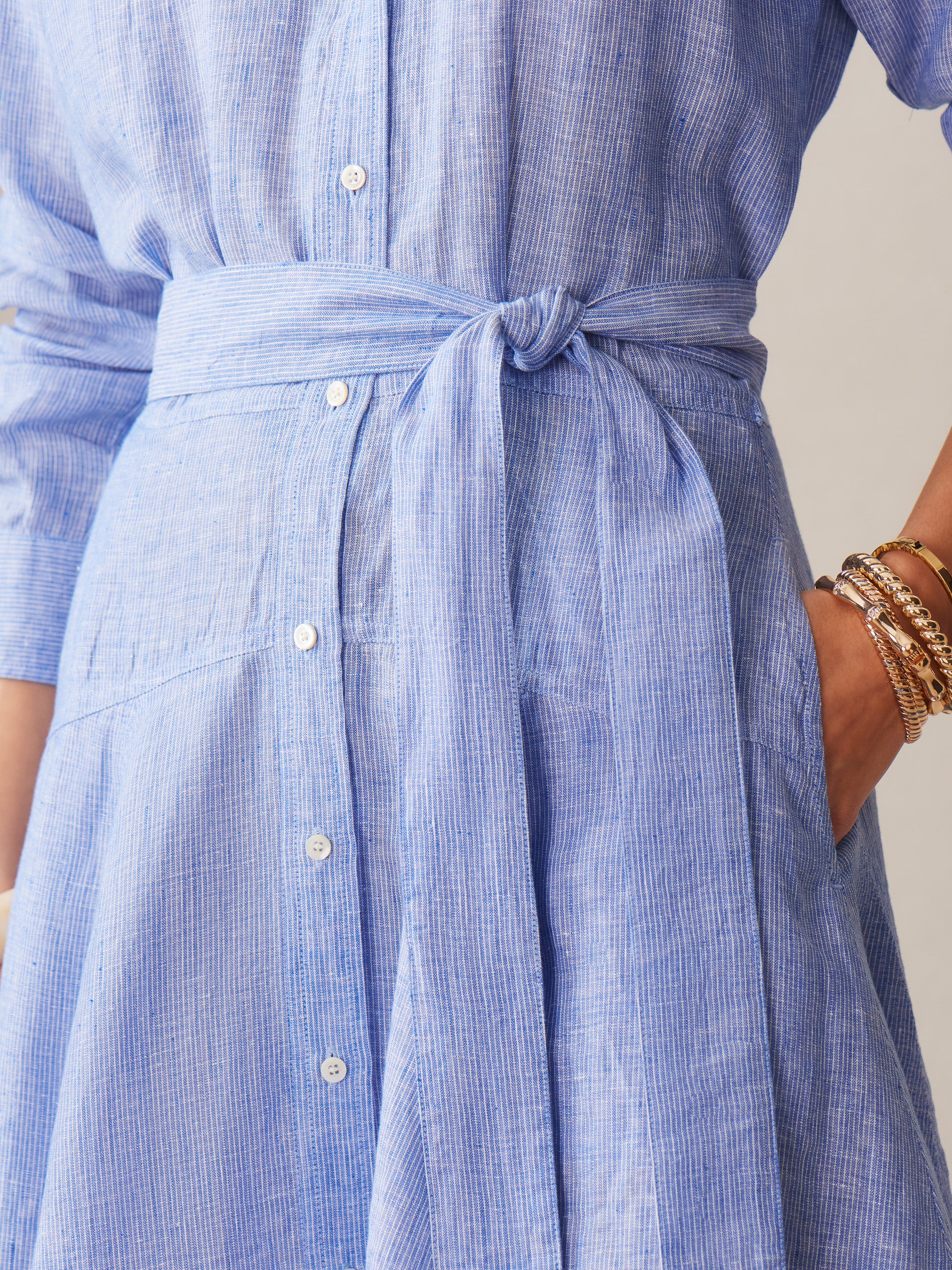Close-up of a woman wearing the Mary Linen Dress in Stripe by J.McLaughlin, featuring a tied waist belt and fine vertical stripes in pastel blue, showcasing effortlessly stylish, enduring designs crafted with innovative fabrics for a legacy of timeless fashion at a destination for defining style. Life, Well-Lived.