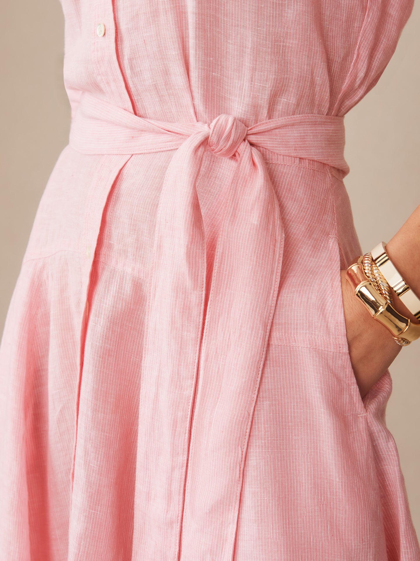 Close-up of a pink striped Mary Linen Dress in Stripe by J.McLaughlin featuring a tied waist belt and a hand resting in the dress pocket, showcasing effortlessly stylish, enduring designs with innovative fabrics.