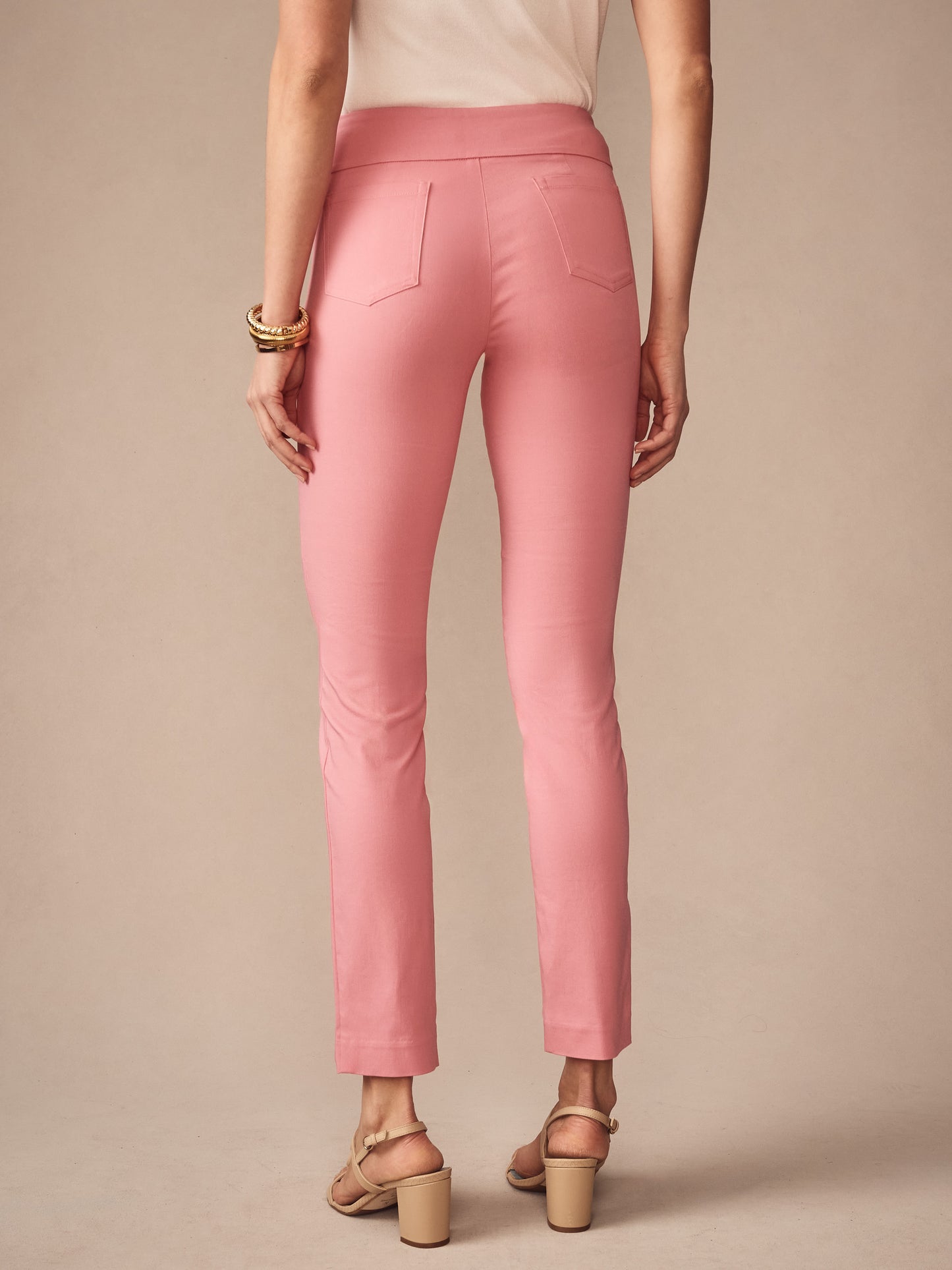 A woman wearing J.McLaughlin Masie Pants in soft pink, styled with neutral sandals and a white top, showcasing effortlessly stylish, enduring designs with innovative fabrics.