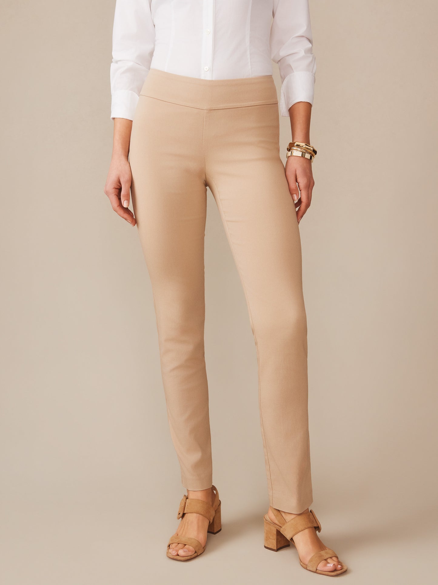 Woman wearing beige Masie Pants and tan heeled sandals paired with a white shirt and gold bracelets, showcasing effortlessly stylish and enduring designs by J.McLaughlin, a destination for defining style. Life, Well-Lived.