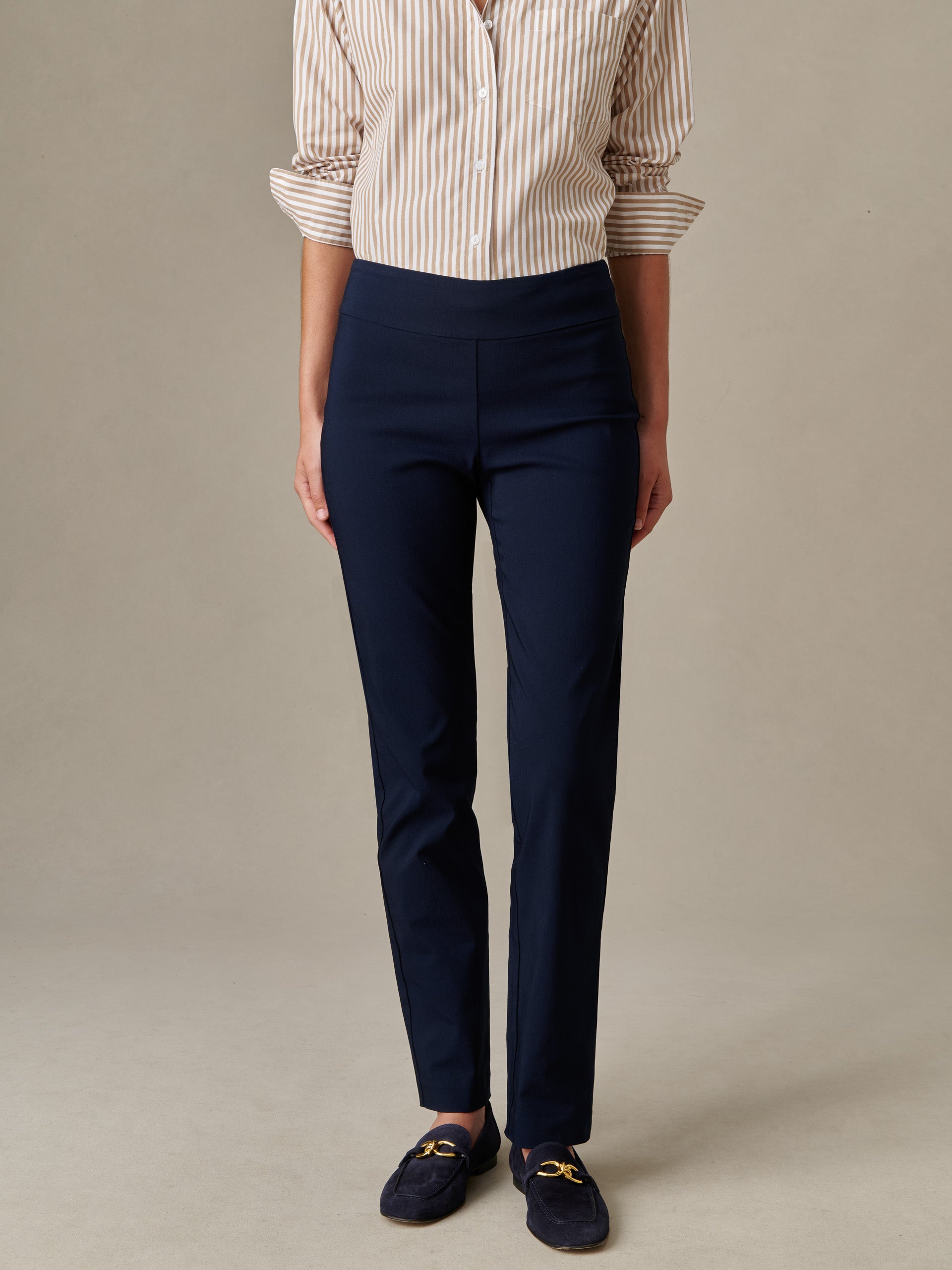 A person wearing navy Masie Pants paired with a beige and white striped shirt and navy loafers, showcasing J.McLaughlin’s effortlessly stylish and enduring design.
