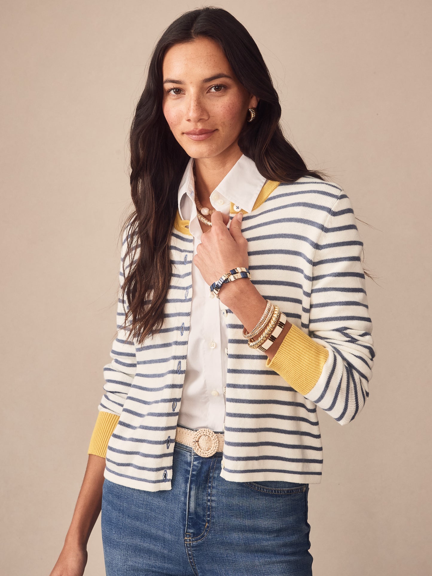 Woman wearing the Matilda Cardigan in Stripe by J.McLaughlin, featuring nautical blue and white stripes with mustard yellow accents on cuffs and collar, styled with a white blouse and denim jeans, showcasing effortlessly stylish, enduring designs with innovative fabrics for a legacy of timeless fashion. A destination for defining style. Life, Well-Lived.