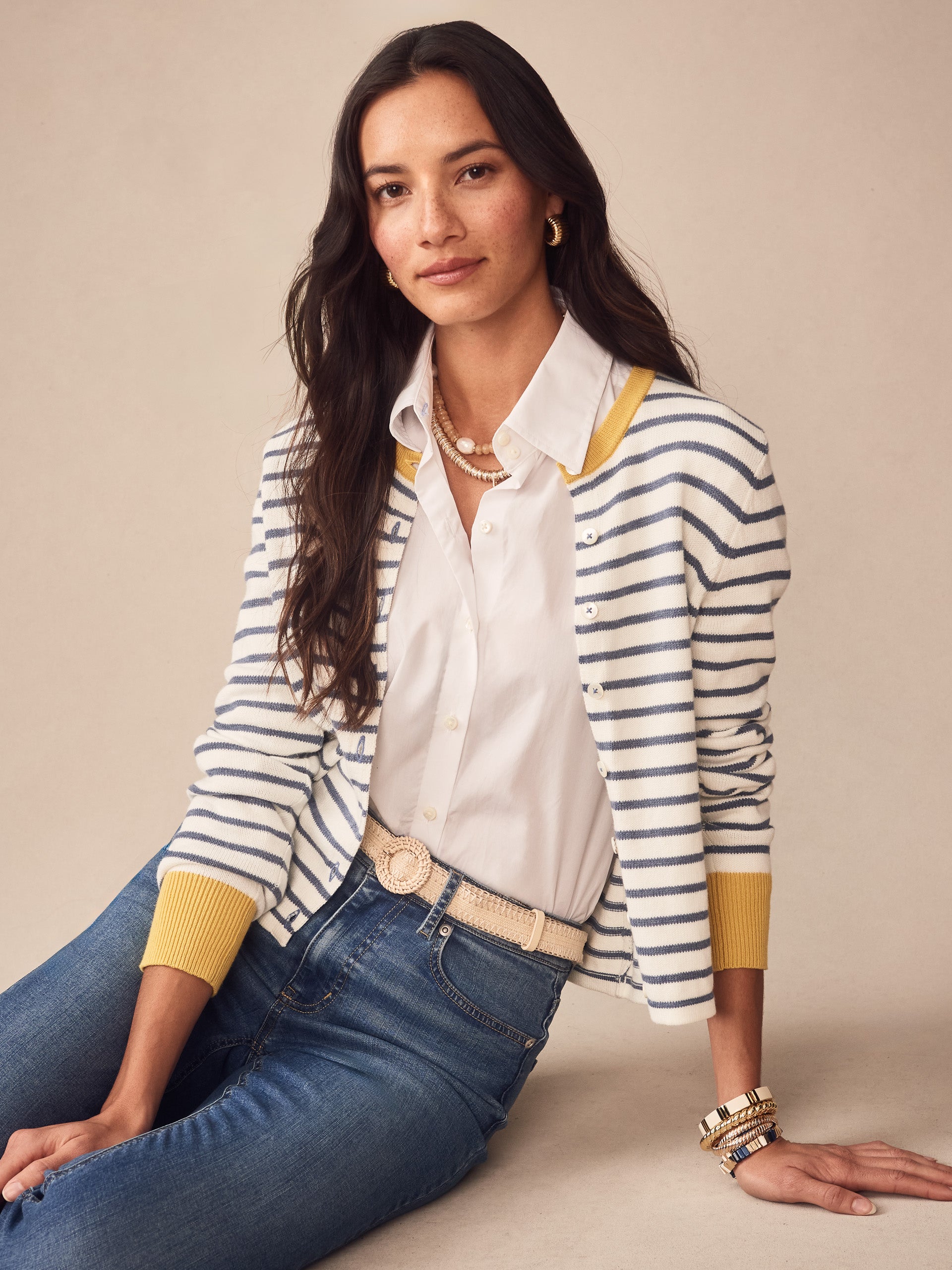 Woman wearing a Matilda Cardigan in Stripe by J.McLaughlin, styled with a white blouse and jeans, showcasing effortlessly stylish layering with innovative fabrics and enduring designs.