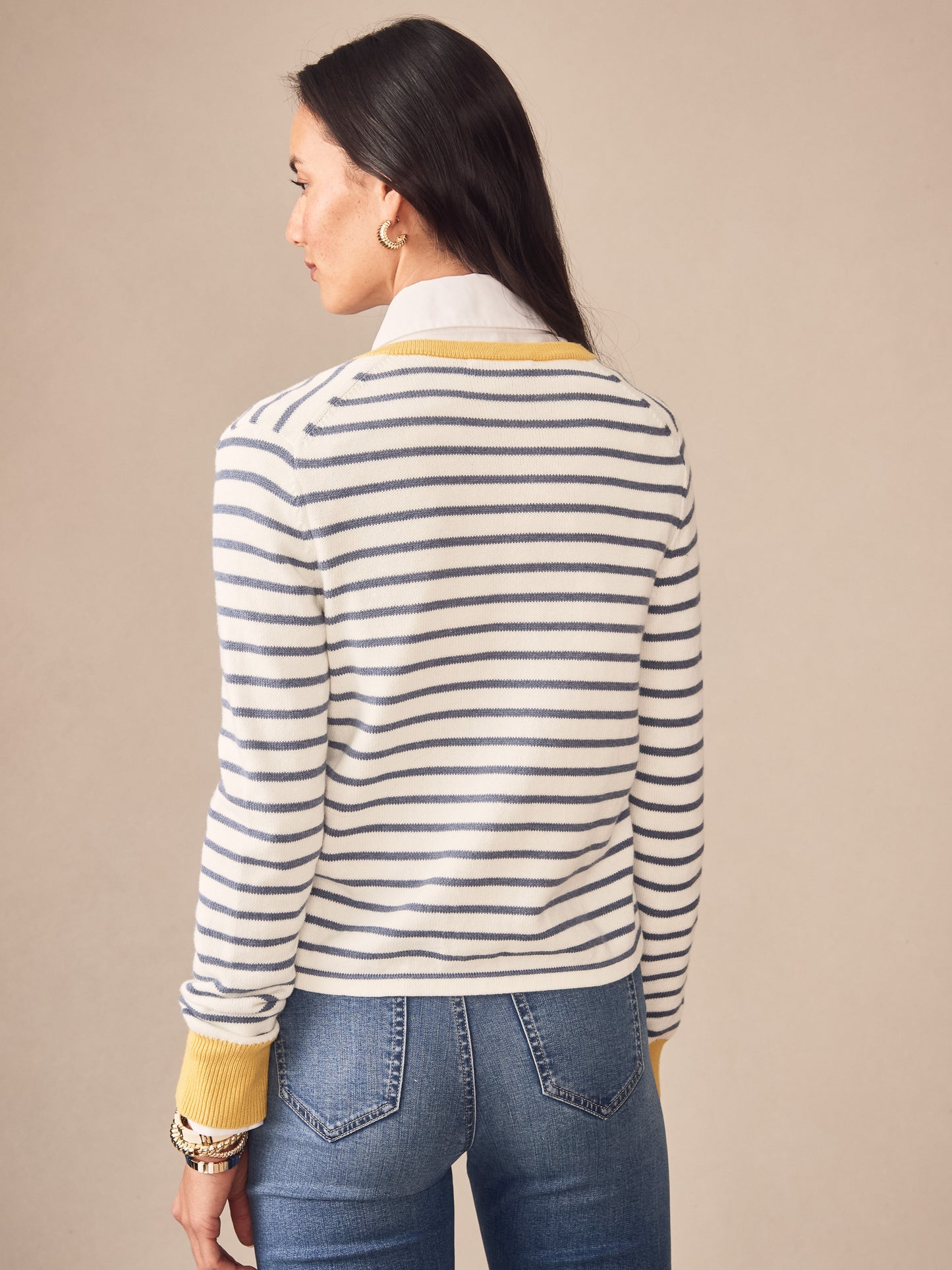 A woman models the Matilda Cardigan in Stripe by J.McLaughlin, featuring classic blue stripes and mustard yellow accents on cuffs and neckline, showcasing effortlessly stylish, enduring designs and innovative fabrics in a legacy of timeless fashion. A destination for defining style. Life, Well-Lived.