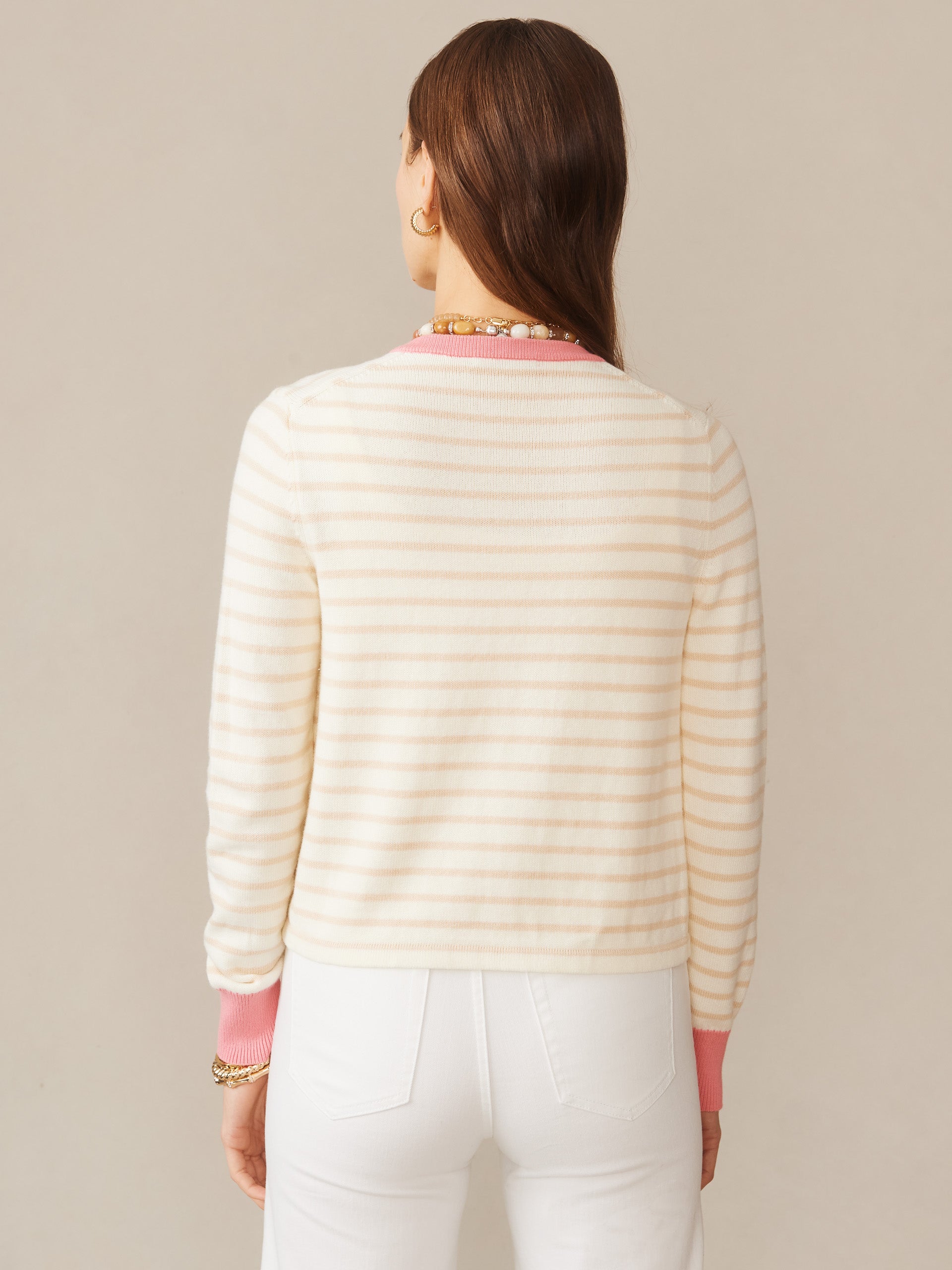 A rear view of a woman wearing the Matilda Cardigan in Stripe by J.McLaughlin, featuring soft neutral stripes with pink accents at the collar and cuffs, effortlessly stylish for enduring designs in versatile sweaters.