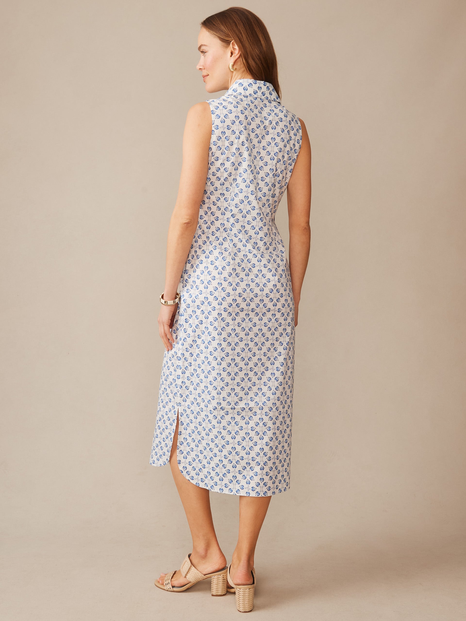 A woman models the Orla Sleeveless Linen Dress in Mythic Floral Geo by J.McLaughlin, showcasing its timeless design, enduring style, and airy linen fabric in a softly patterned blue and white print.
