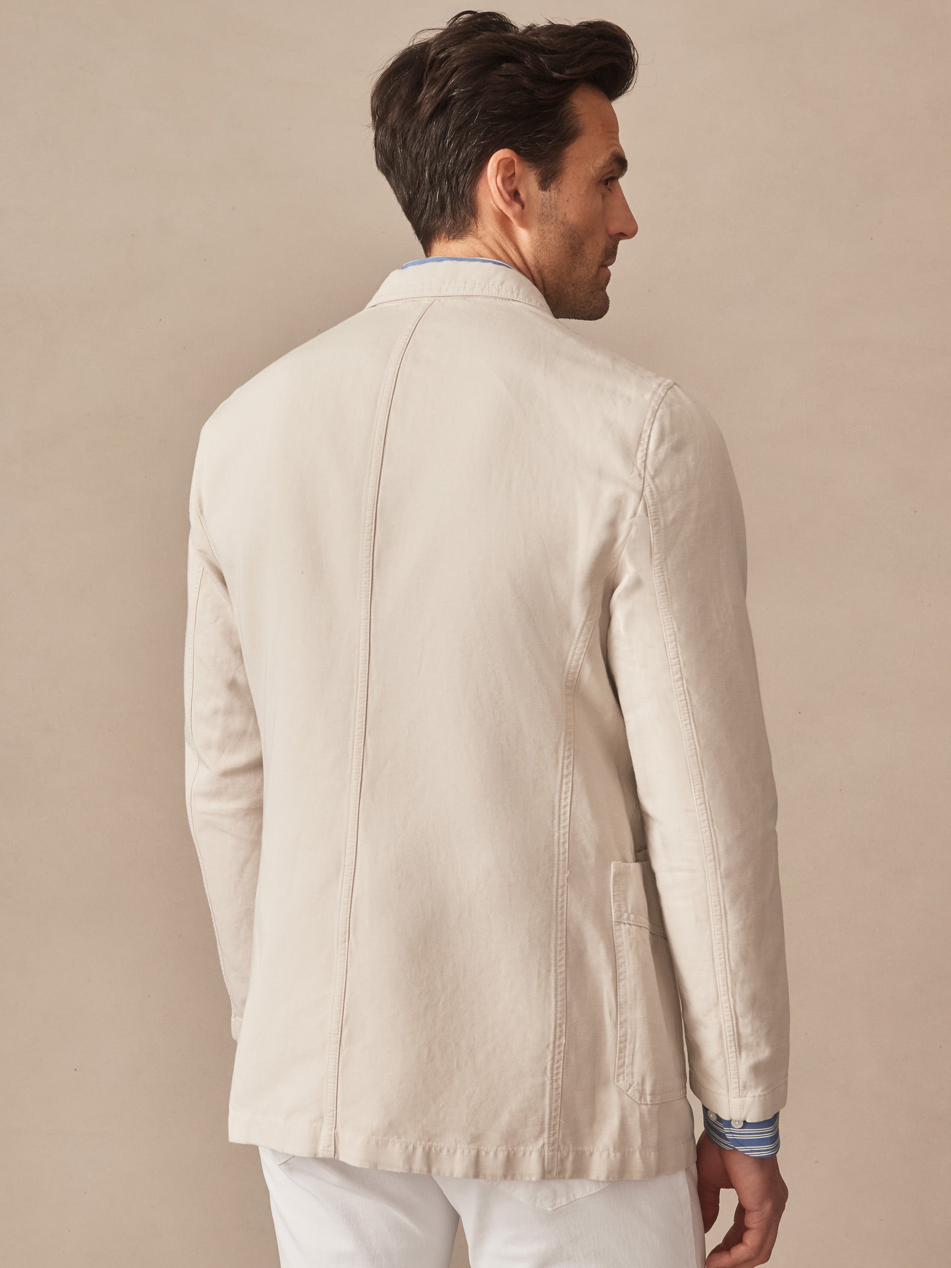 Man wearing the Charlestown Jacket by J.McLaughlin in a soft, neutral tone showcasing impeccable craftsmanship and innovative fabric for effortlessly stylish, enduring designs.